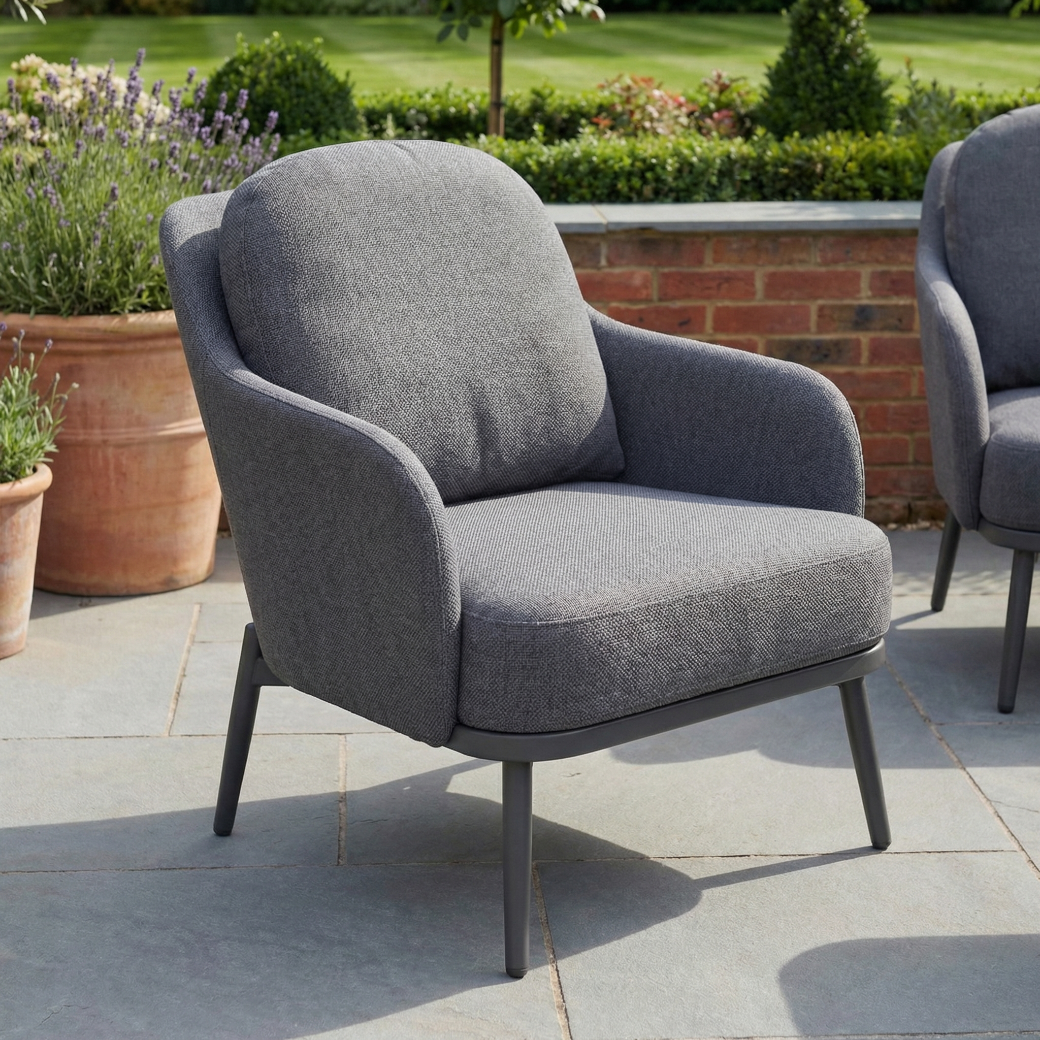 The Alva 3 Seat Sofa Dining Set with Rising Table in Grey, from a stylish garden collection, is arranged on a stone patio with lush greenery as the backdrop.