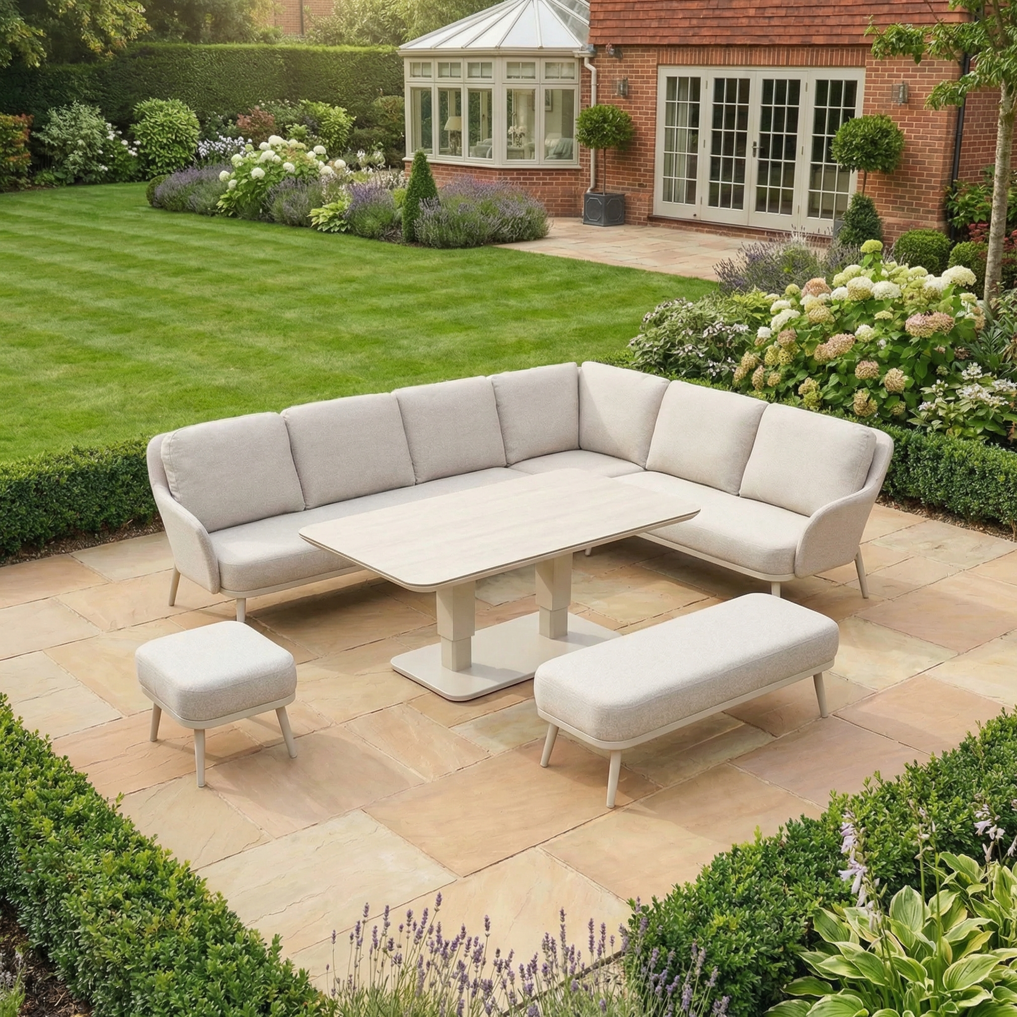 Outdoor patio featuring the Alva Corner Dining Set with Rising Table in Fawn (Right Hand), including a beige sectional, bench, and stool—ideal garden furniture surrounded by green lawn and landscaped garden.