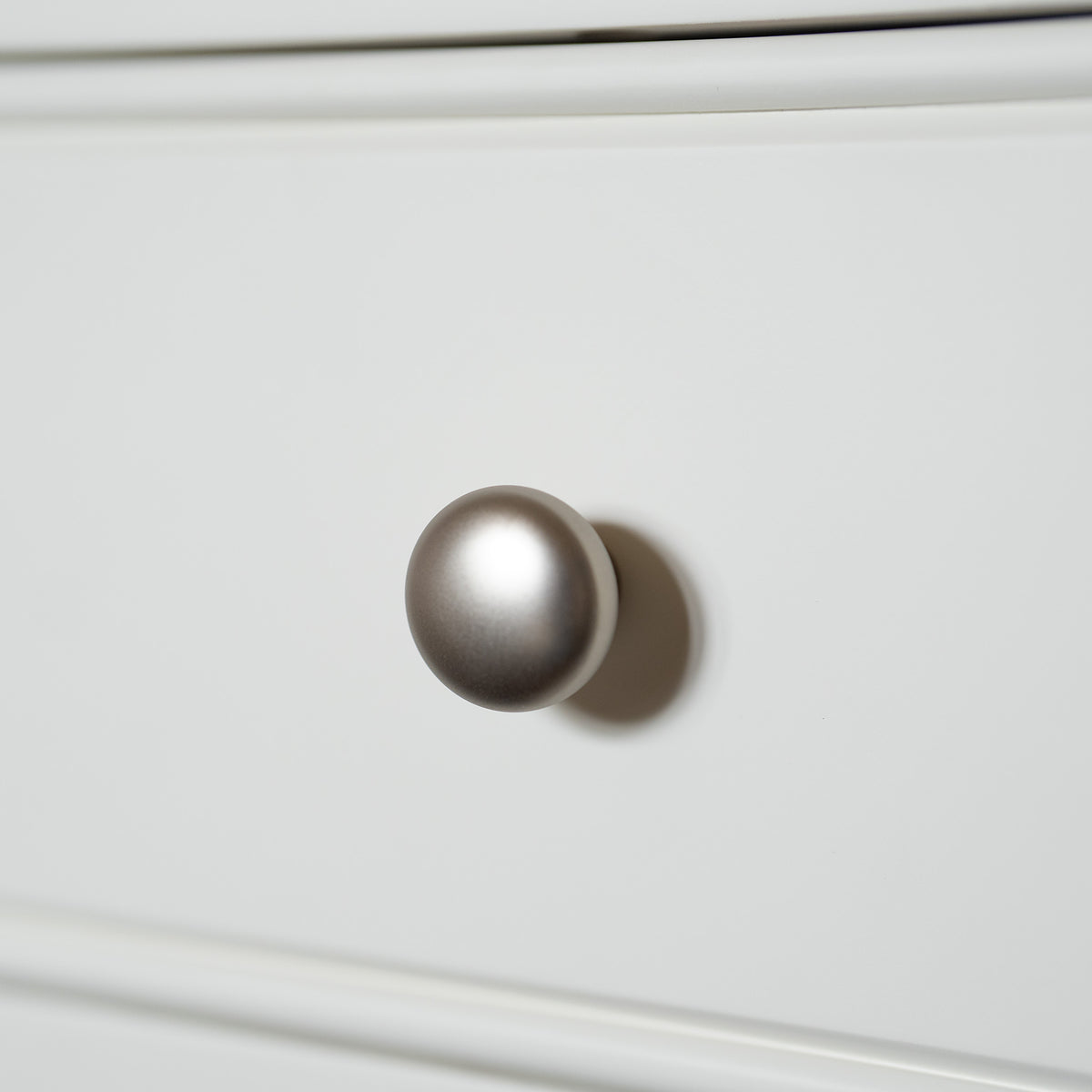 Close-up of a round silver drawer knob on a smooth white drawer front, highlighting the refined detail of the Amberley Bedside Table in Warm White—a perfect example of modern country furniture.