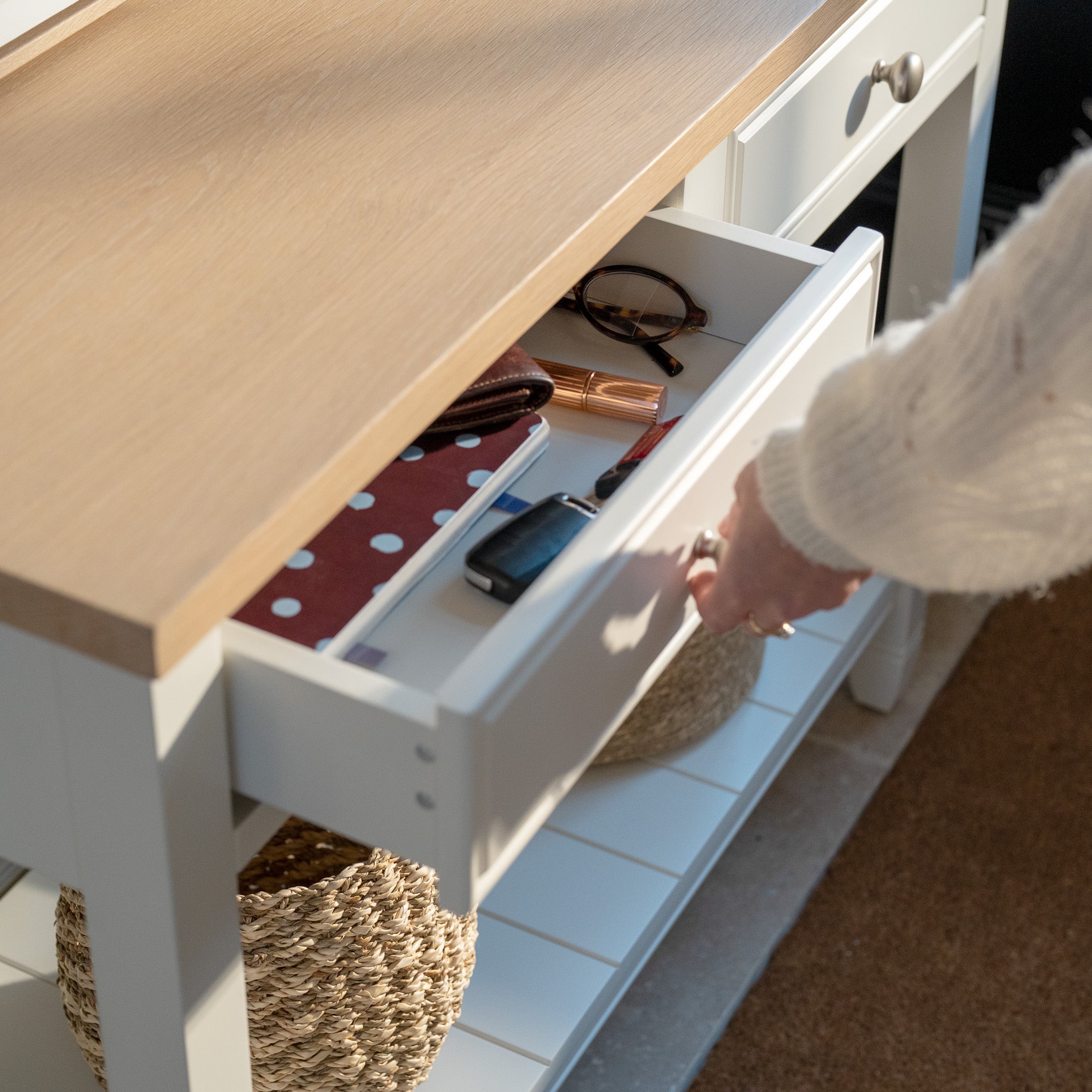 Someone opens the Amberley 2 Drawers Console Table in Warm White, showing glasses, notebooks, keys, and a phone neatly stored on its stylish oak top in farmhouse style.
