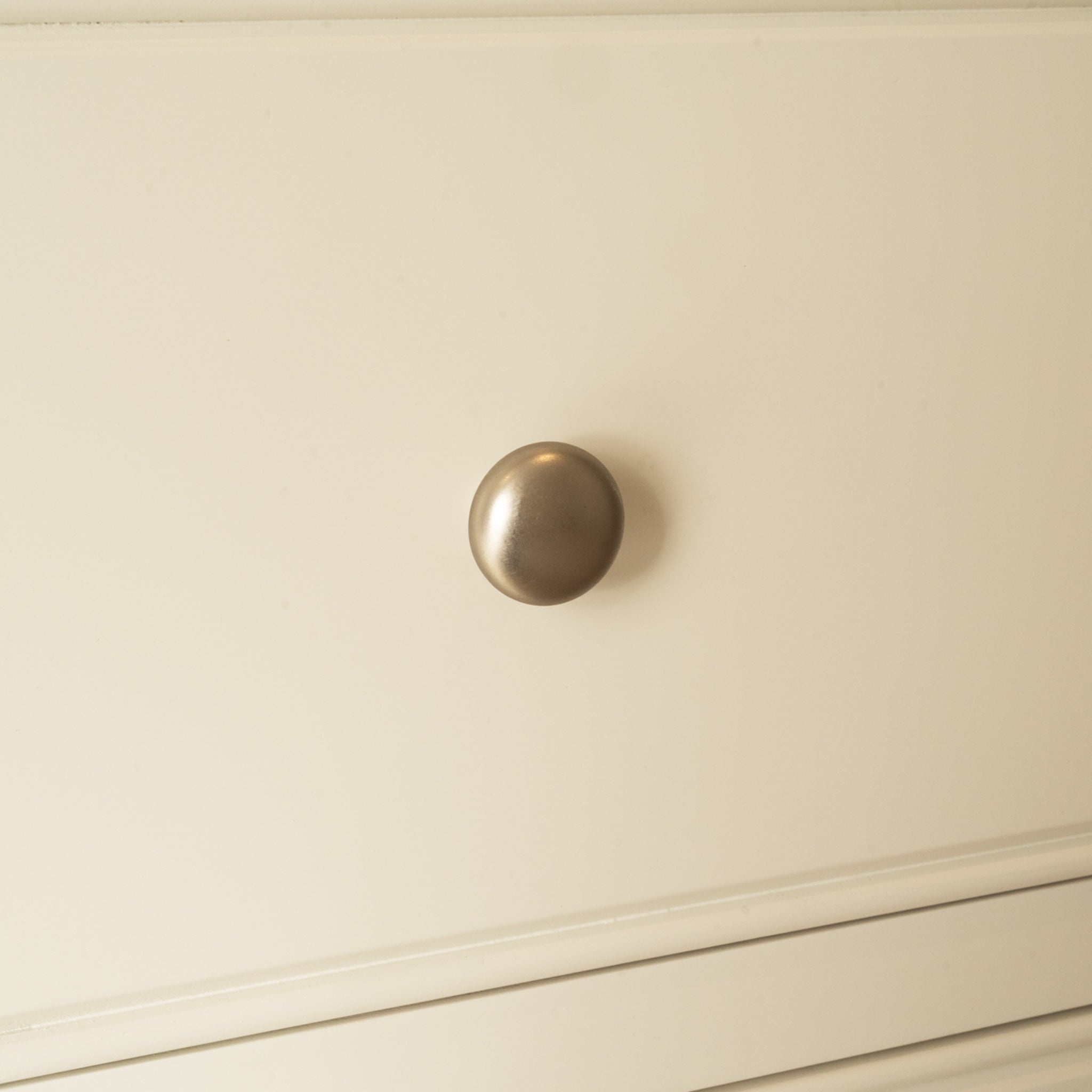 Close-up of a round metallic knob on the Amberley 3 Over 4 Chest of Drawers in Warm White, featuring an elegant oak top.