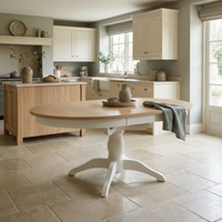 Bright kitchen featuring the Amberley 4-6 Seater Round Extending Dining Table in Warm White, complemented by white cabinets, an island, and large windows flooding the space with natural light.