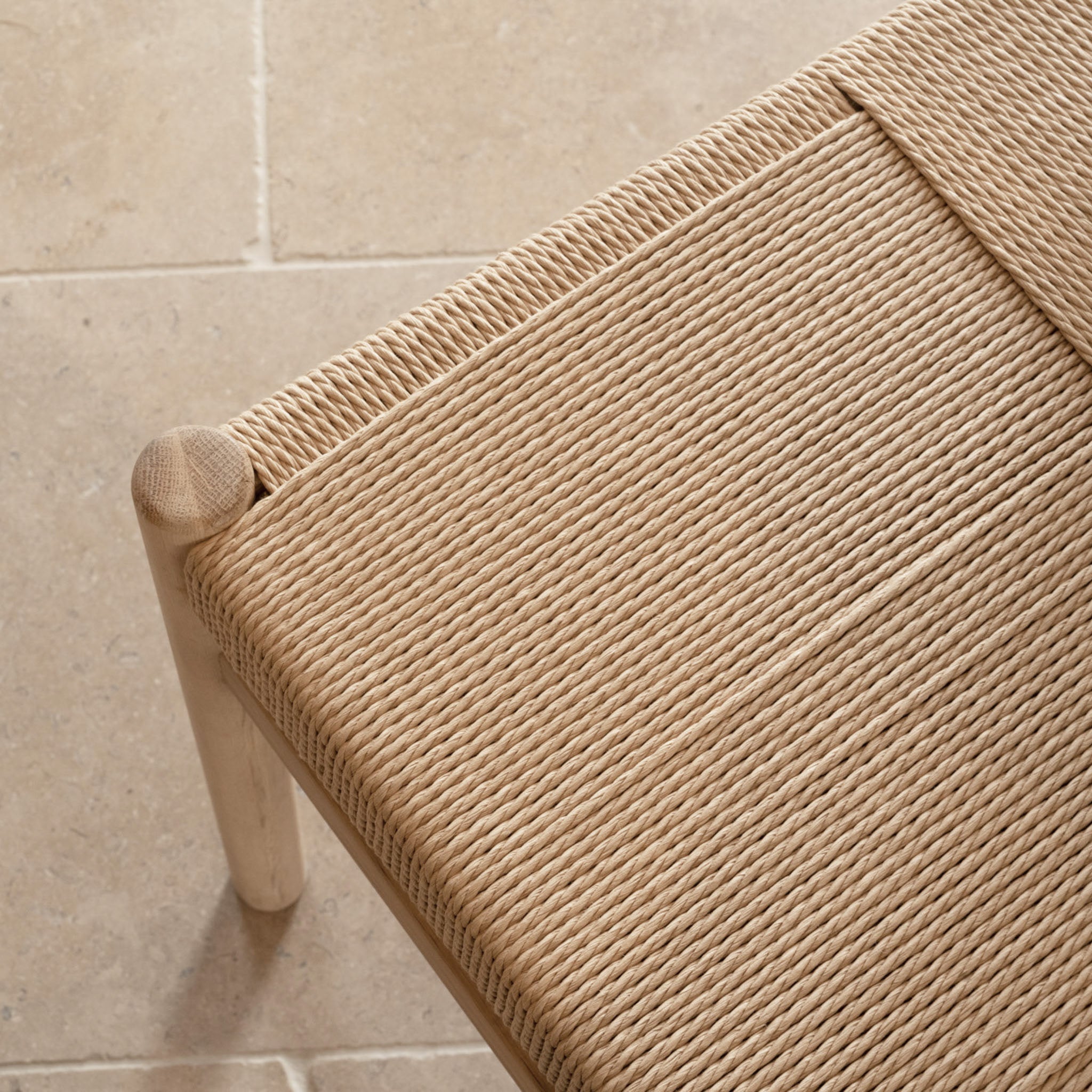 Close-up of a woven rope seat on a wooden chair beside the Amberley 4-6 Seater Round Extending Dining Table in Light Oak, set on beige tiled flooring.