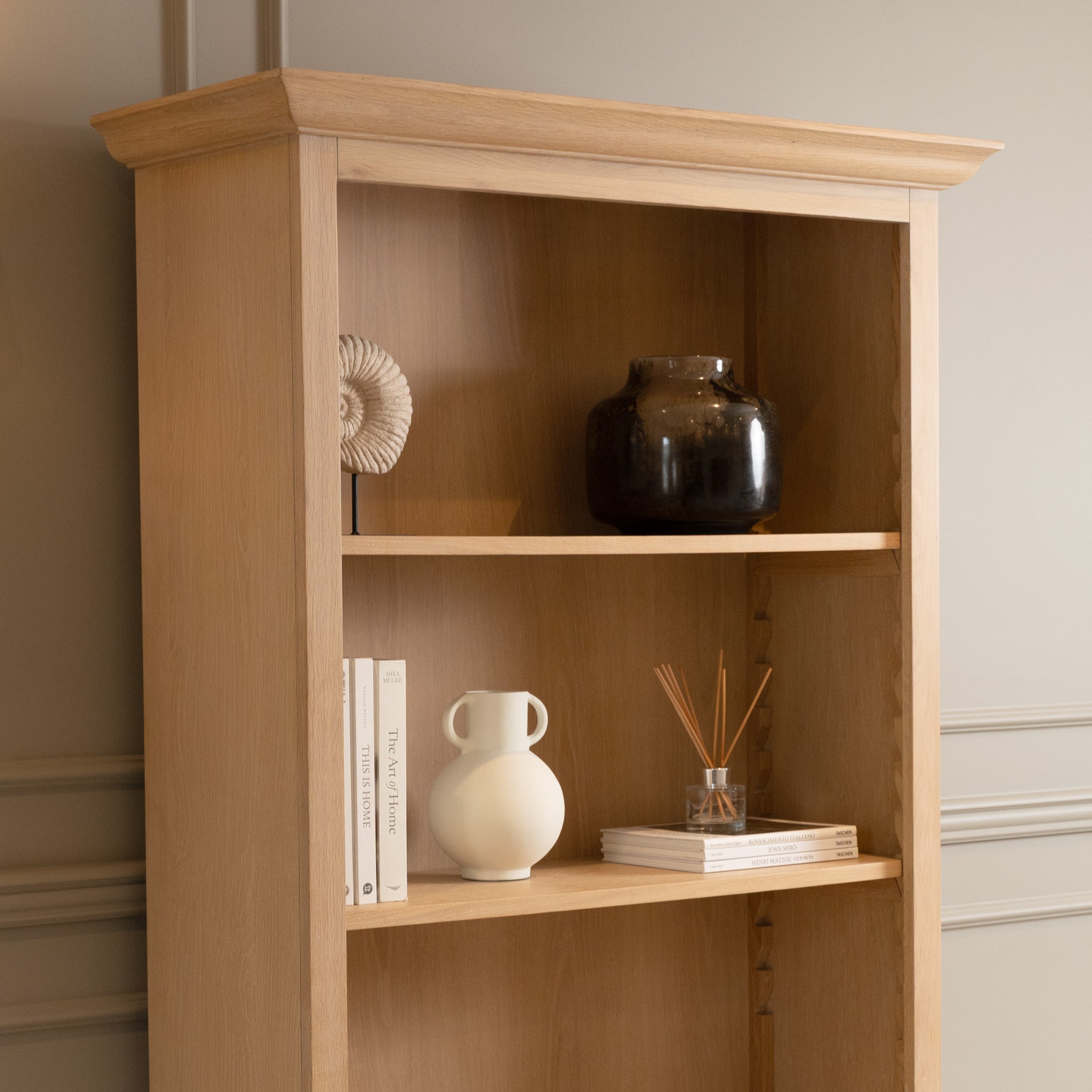 The Amberley Large Bookcase in Light Oak showcases books, a vase, a sculpture, a dark jar, and reed diffusers in a modern country style.
