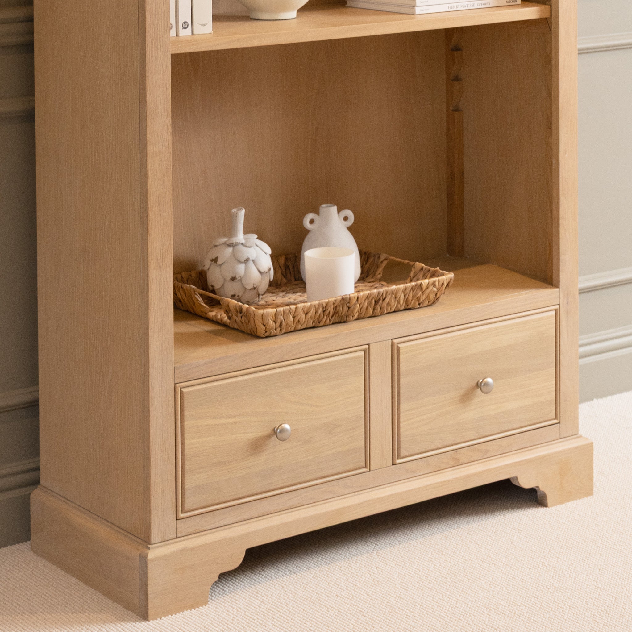 The Amberley Large Bookcase in Light Oak features two drawers and ample storage, ideal for displaying trays with decorative vases and candles—perfect for a modern country look.