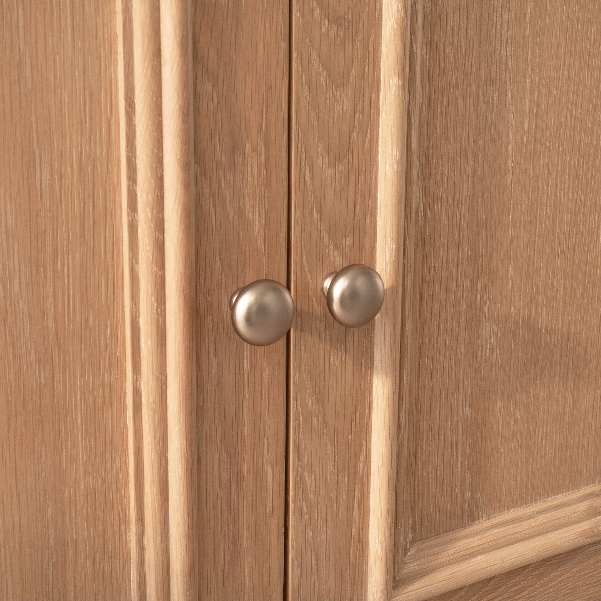 Close-up of two round metal knobs on the wooden cabinet doors, highlighting the light wood grain texture of the Amberley Large 4 Door 2 Drawers Sideboard in Light Oak.