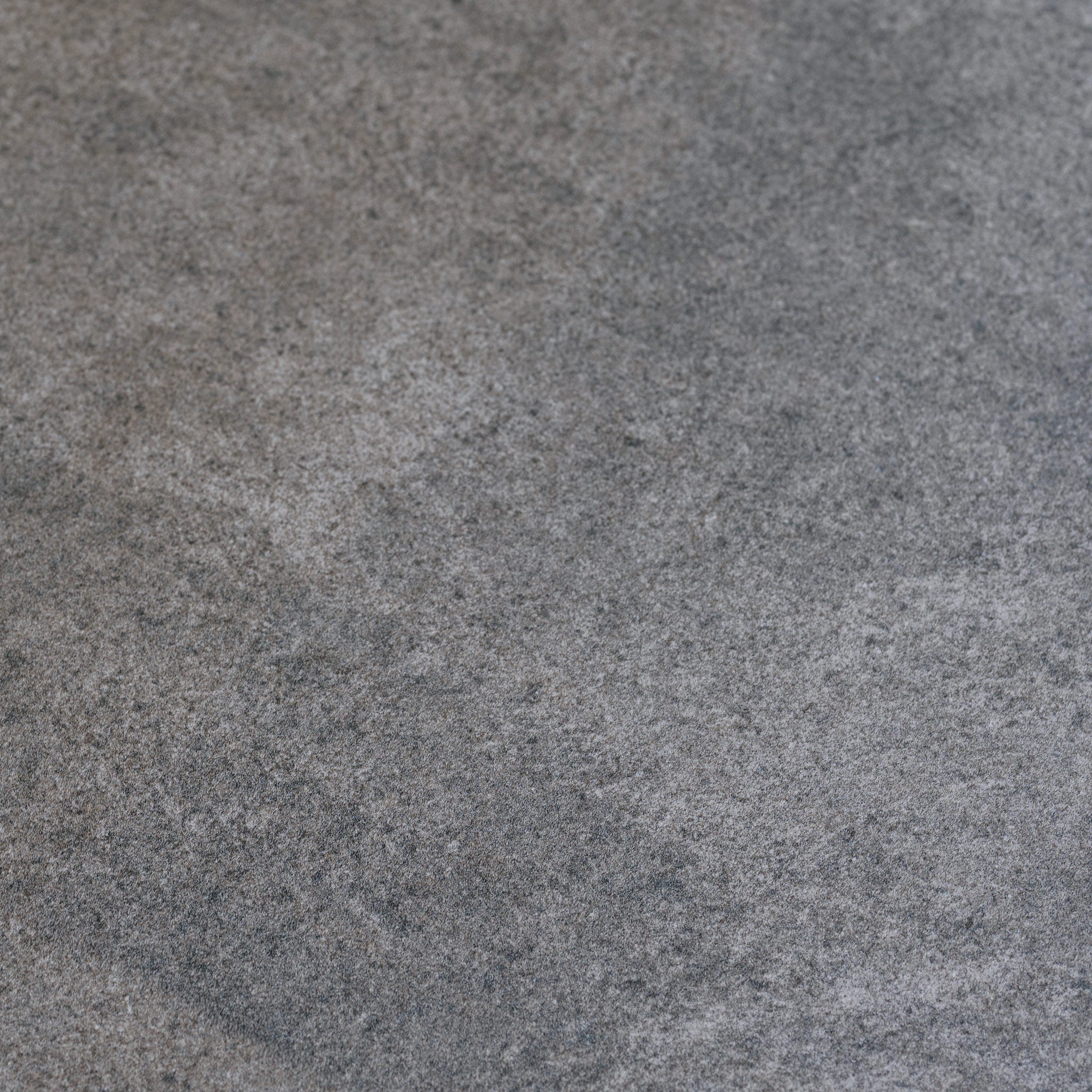 The Andora Round Side Table in Weathered Brown features a slightly rough, textured gray concrete surface with subtle color variations—perfect as a coffee table or paired with eucalyptus wood accents.