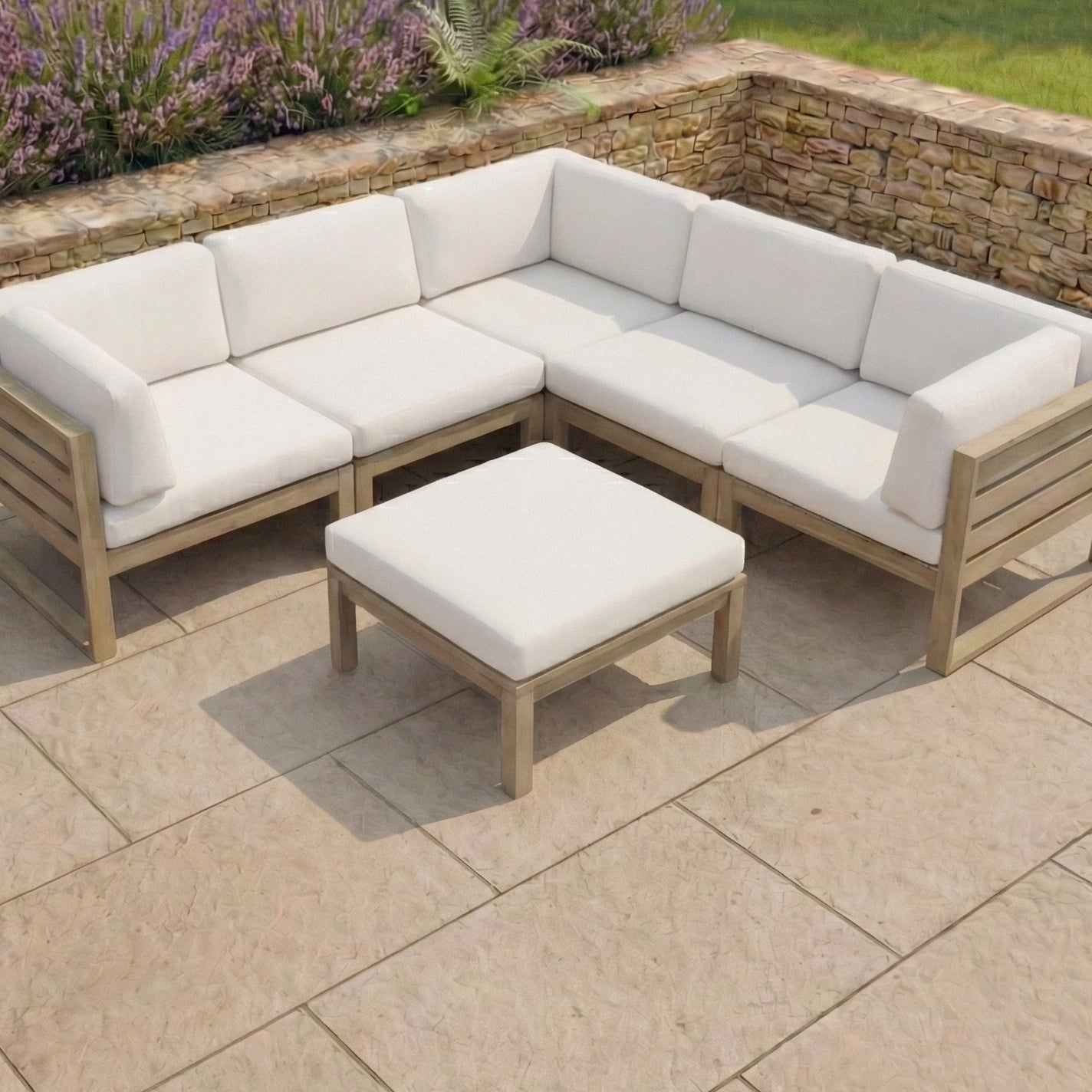 Outdoor patio set featuring a white cushioned sectional sofa and the Andora Coffee Table & Footstool in Weathered Brown and Linen, set on a tiled patio next to a stone wall.