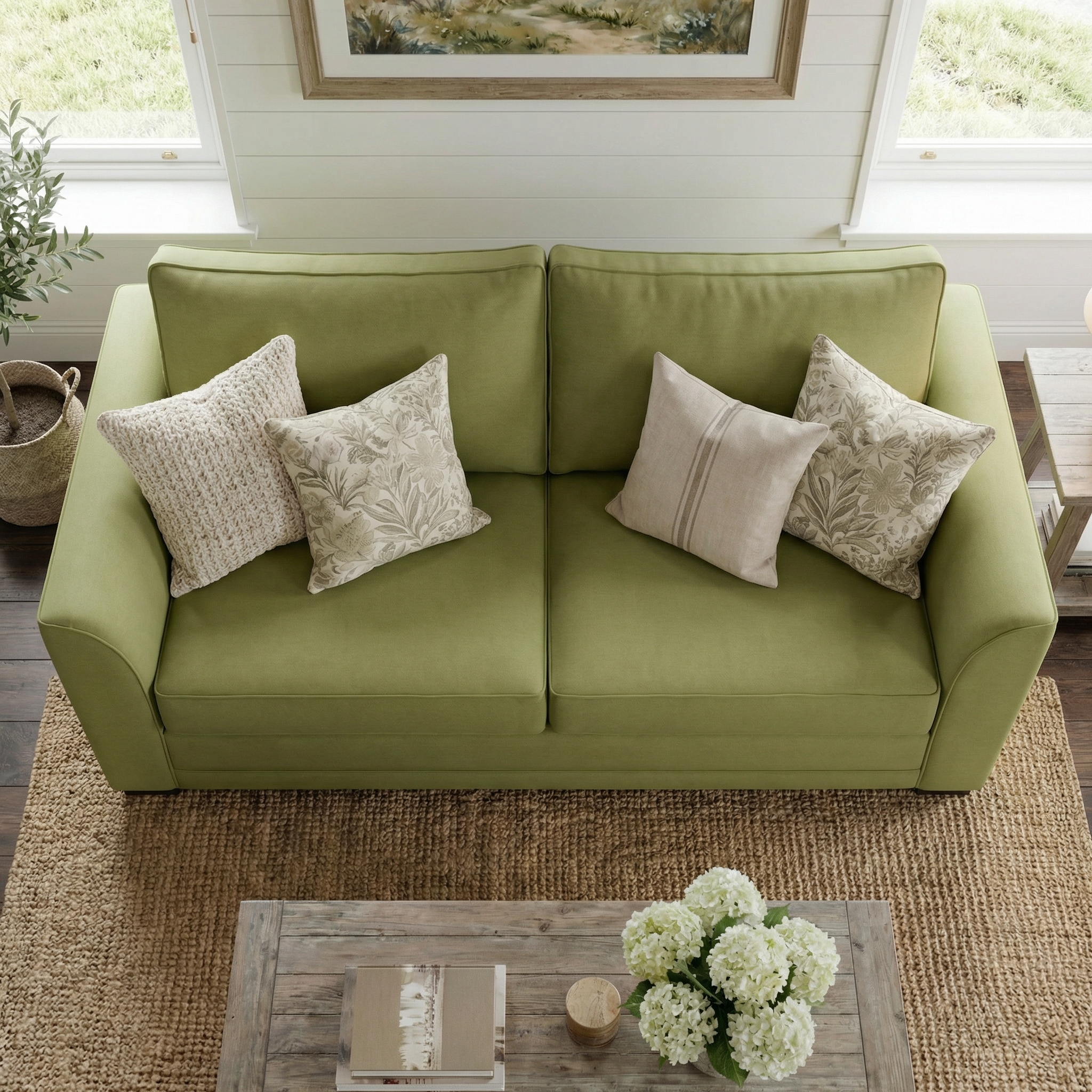 Ardley 3 Seat Sofa Bed in Olive with four beige throw pillows, placed beside a wooden coffee table topped with white flowers and a woven rug.