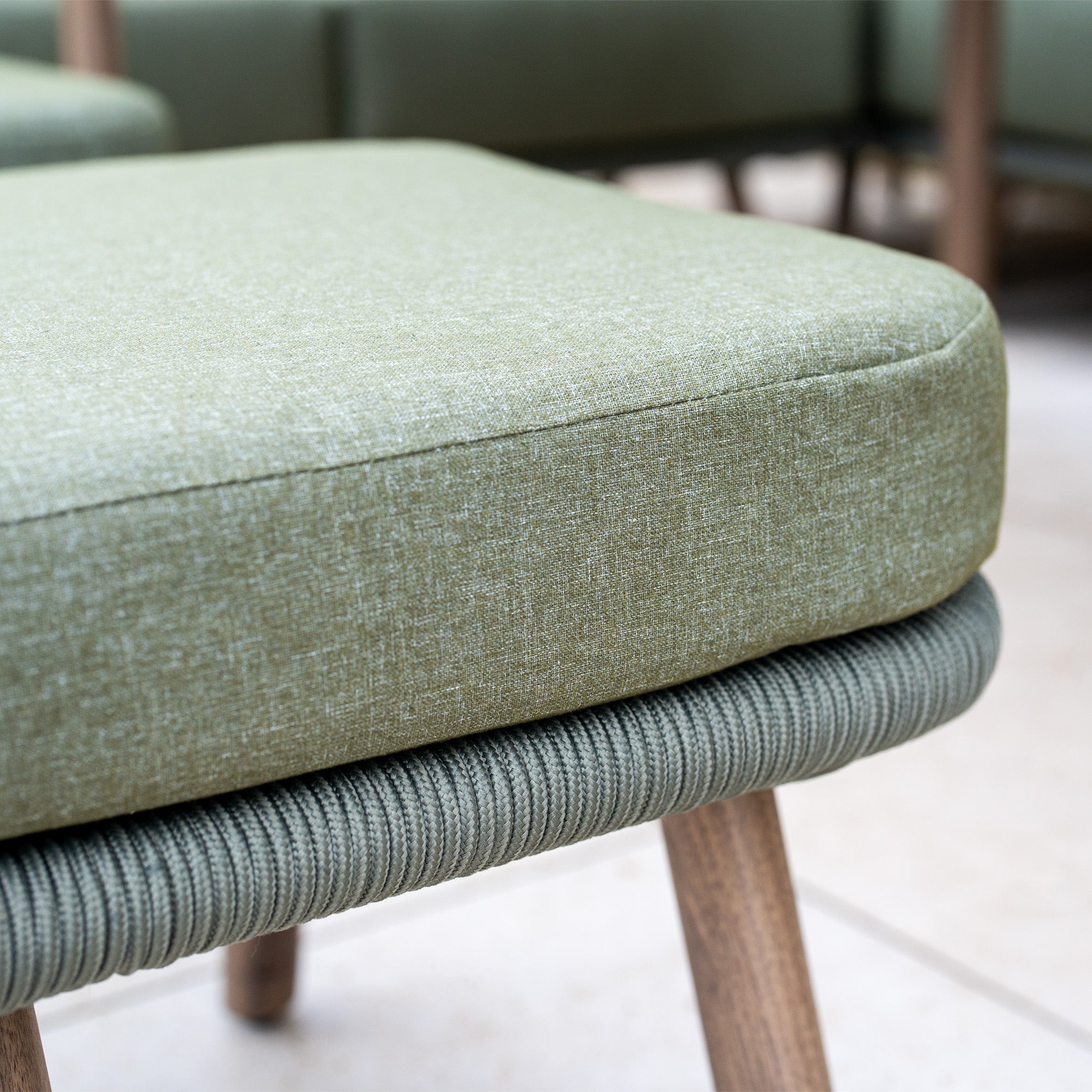 Close-up of a green cushioned chair with wooden legs and textured fabric, part of the Ascot Corner Dining Set in Forest Green—ideal as weather-resistant garden furniture.