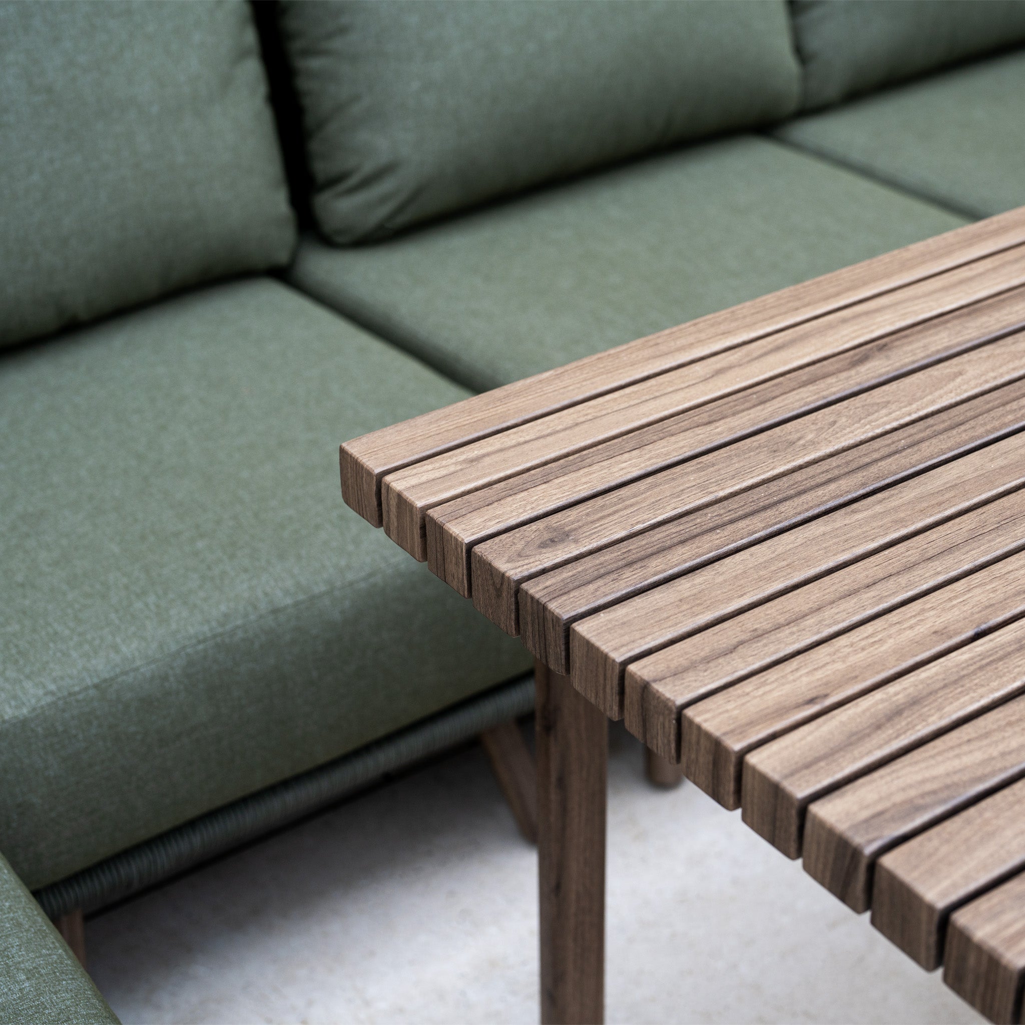 Close-up of the wooden slatted table from the Ascot Corner Dining Set with Armchair in Forest Green, placed beside a matching forest green garden sofa.