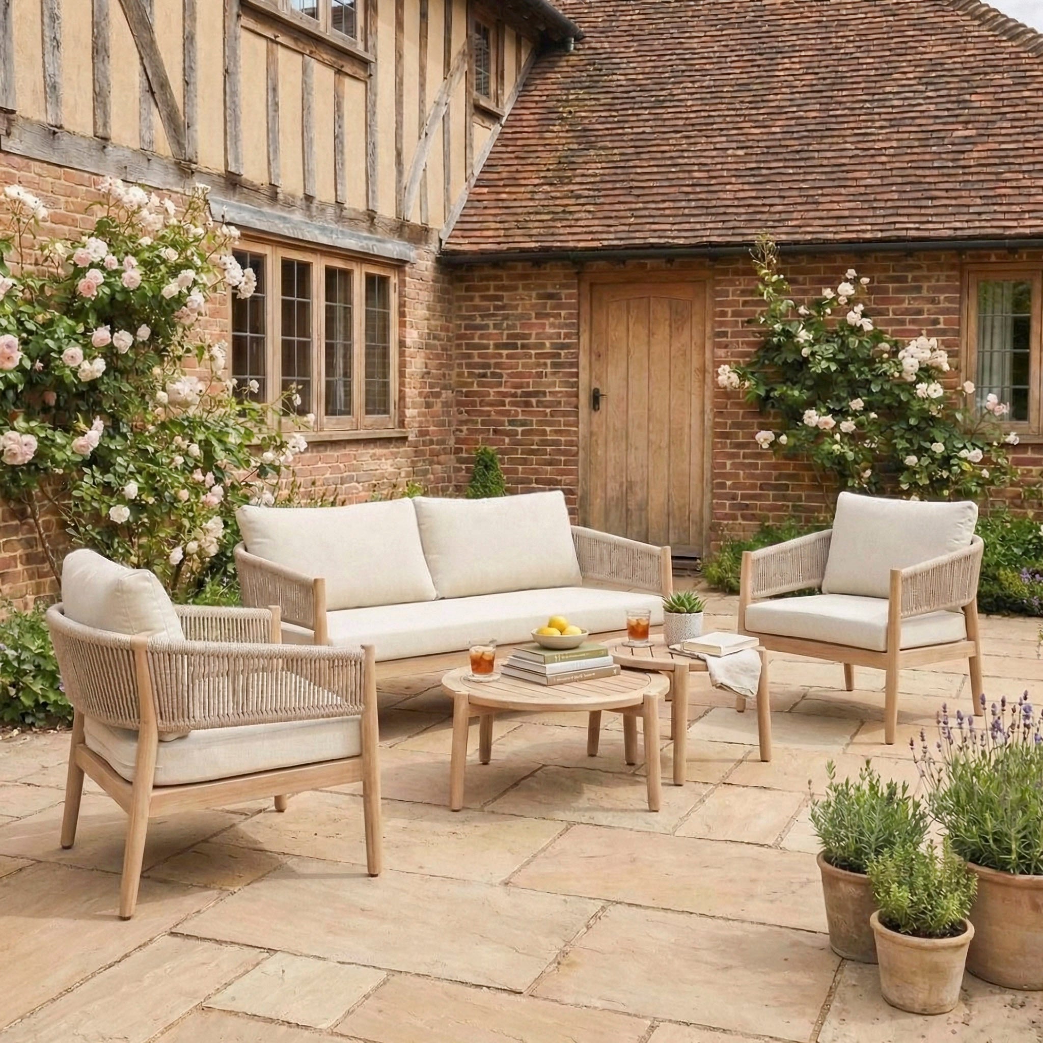 Outdoor patio featuring the Astoria 2 Seat Sofa Set in Ash Grey with beige cushions and a wooden table—ideal for relaxing by a brick house with elegant garden furniture.