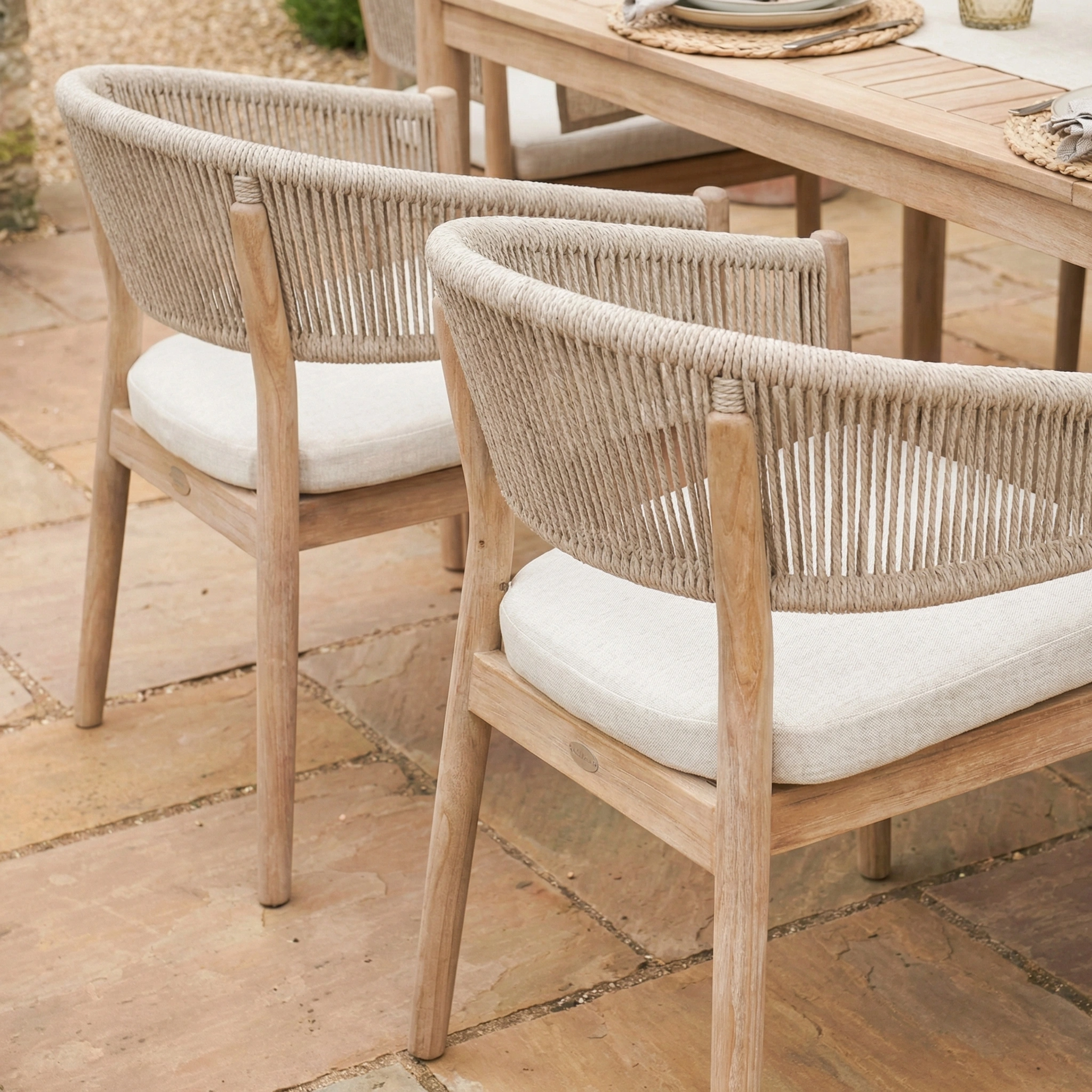 Two wooden patio chairs with woven backs and white cushions sit beside the Astoria 6 Seat Rectangular Dining Set in Ash Grey, perfect for stylish outdoor dining.