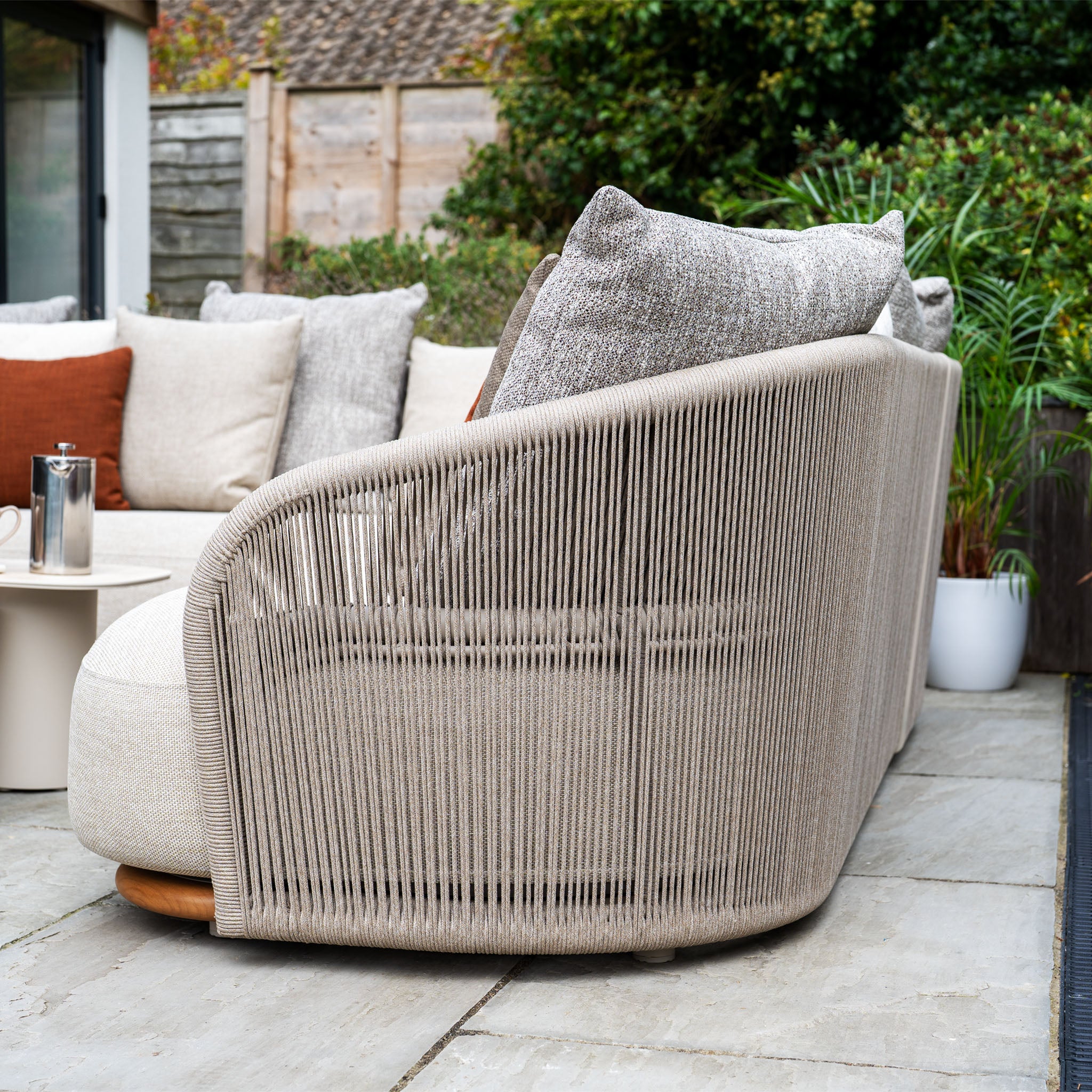 Side view of the Avola Corner Sofa Set in Fawn, a modern outdoor sofa with beige rope accents and neutral, weather-resistant olefin cushions on a patio.