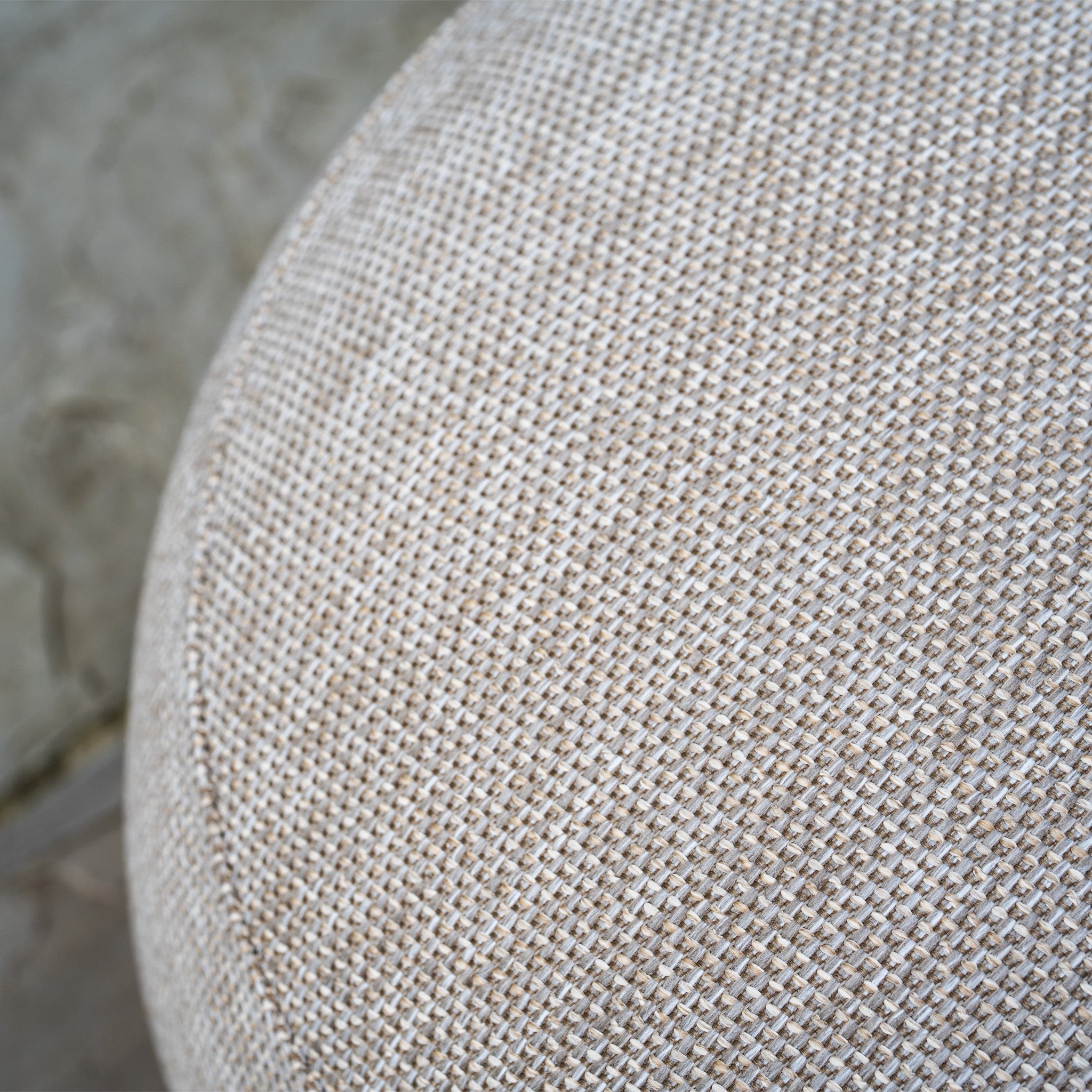 Close-up of textured beige upholstery fabric on a round cushion from the Avola Corner Sofa Set in Fawn, made with weather-resistant olefin, with a blurred background.