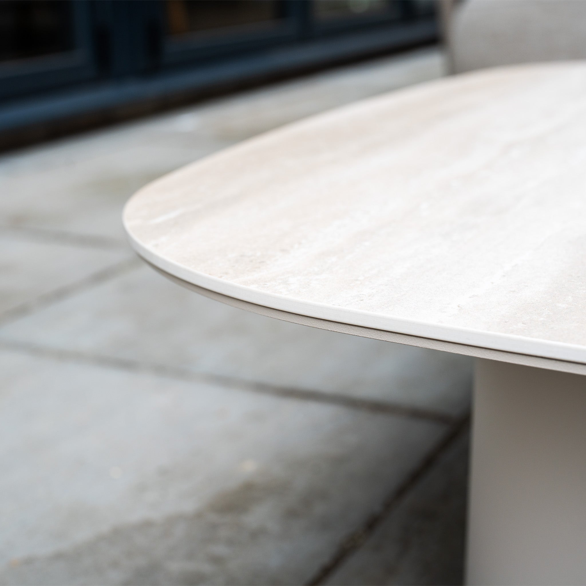 Close-up of a light beige stone tabletop with rounded edge, set on a tiled outdoor patio next to the weather-resistant Avola Corner Sofa Set in Fawn.