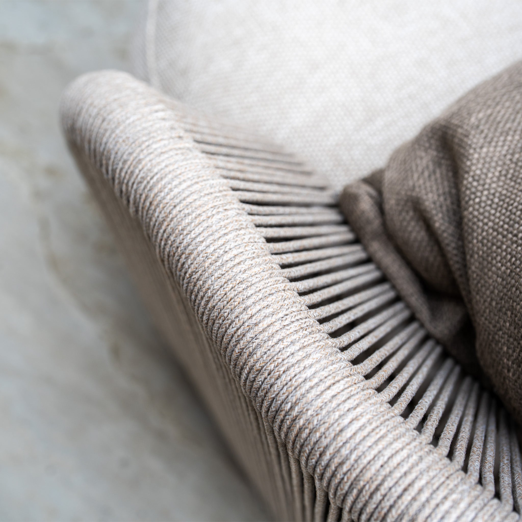 Close-up of a beige woven chair with a brown cushion draped over the seat, perfectly complementing the weather-resistant olefin in our Avola Corner Sofa Set in Fawn for stylish outdoor garden sofa arrangements.