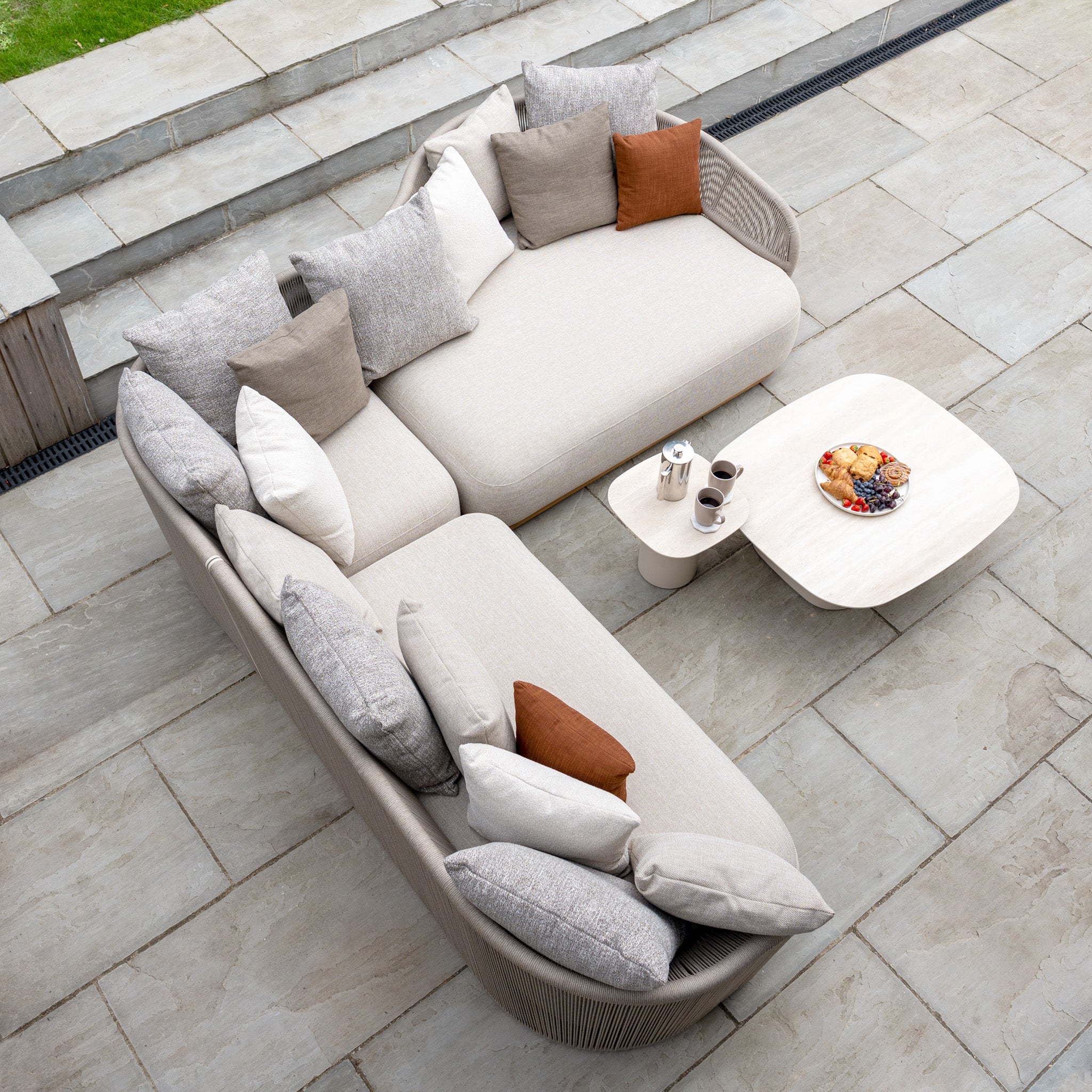 Avola Deluxe Corner Sofa Set in Fawn (Left Hand) features weather-resistant Olefin rope, assorted pillows, and a coffee table—ideal teak and aluminium garden furniture for outdoor gatherings on your patio.