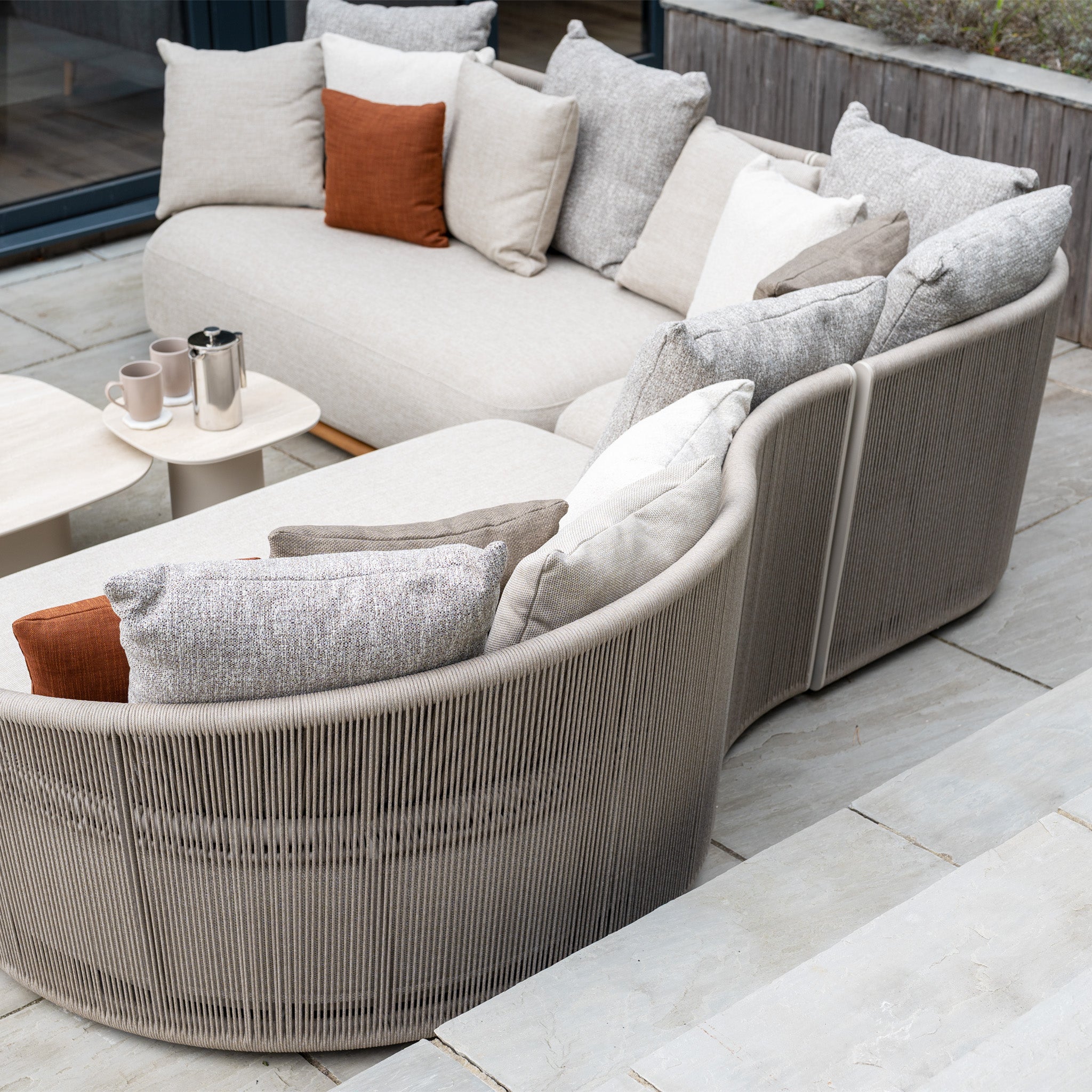 Avola Deluxe Corner Sofa Set in Fawn (Left Hand) with durable, neutral and rust Olefin cushions and a small side table—an inviting, weather-resistant garden set ideal for relaxing outdoors on your patio.