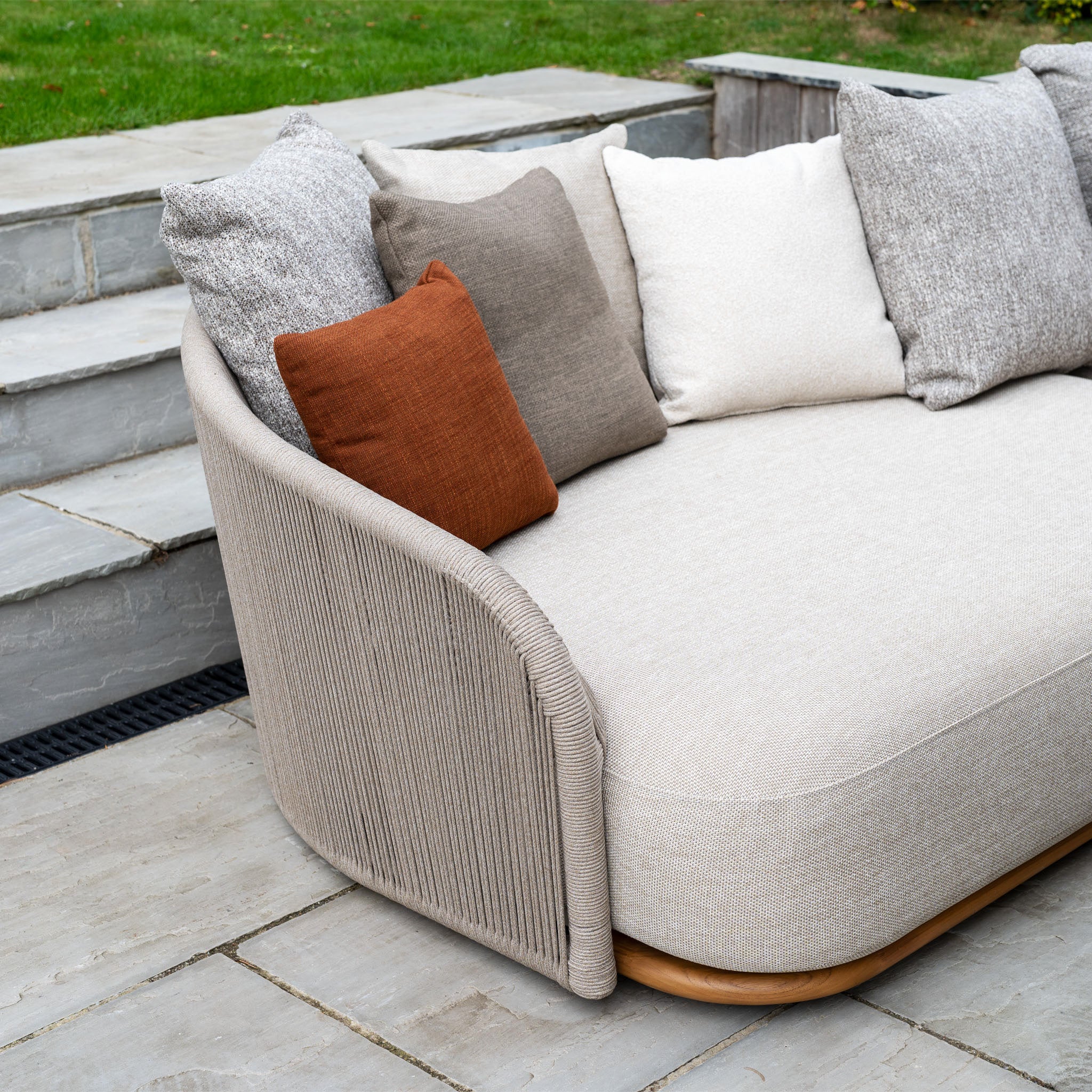 The Avola Deluxe Corner Sofa Set in Fawn (Right Hand) features weather-resistant Olefin rope inspired by premium teak and aluminium furniture, with mixed neutral and brown cushions perfect for a stone patio near garden steps.