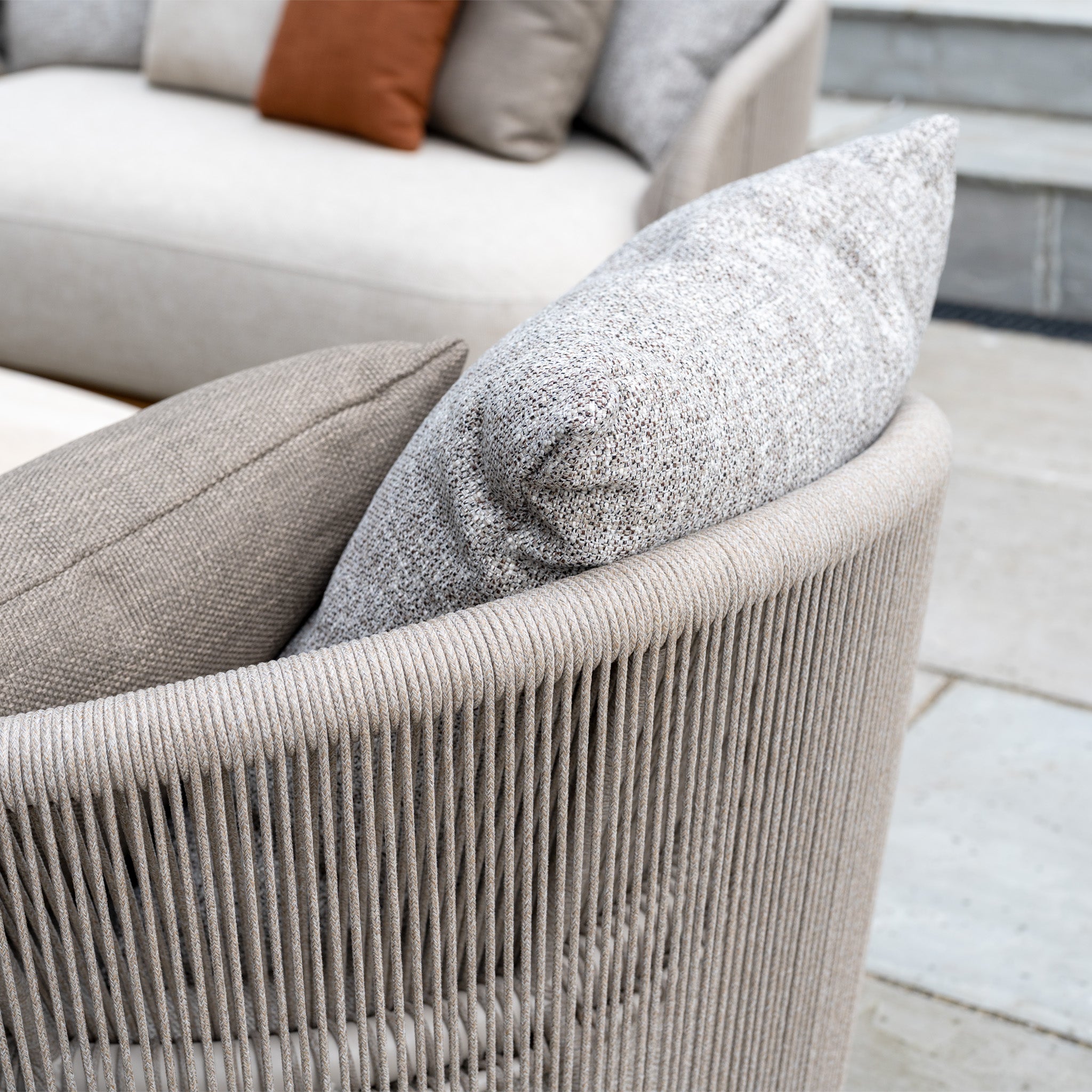 Close-up of the Avola Swivel Armchair in Fawn, featuring weather-resistant Olefin textured cushions and stylish rope detailing on its curved back for outdoor living.