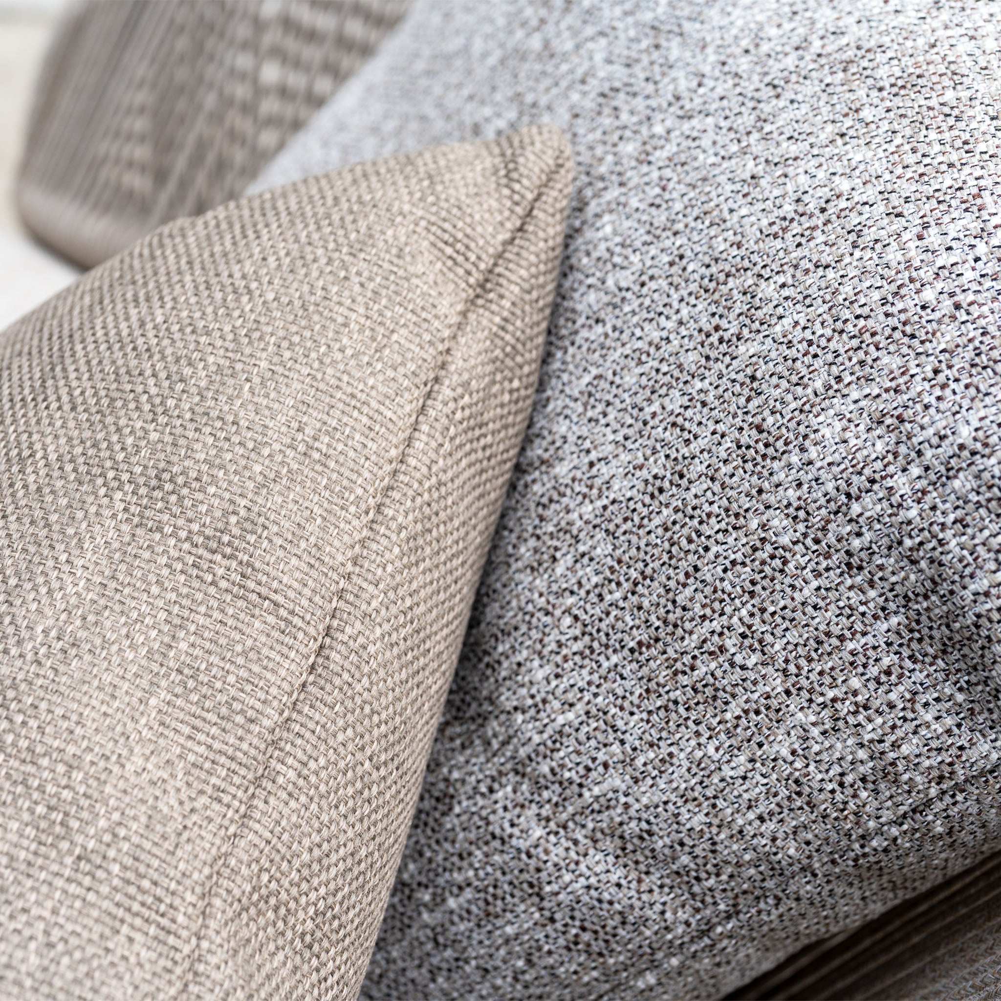Close-up of two textured throw pillows in beige and gray on an Avola Swivel Armchair in Fawn, crafted with weather-resistant Olefin—ideal for your outdoor living setup.
