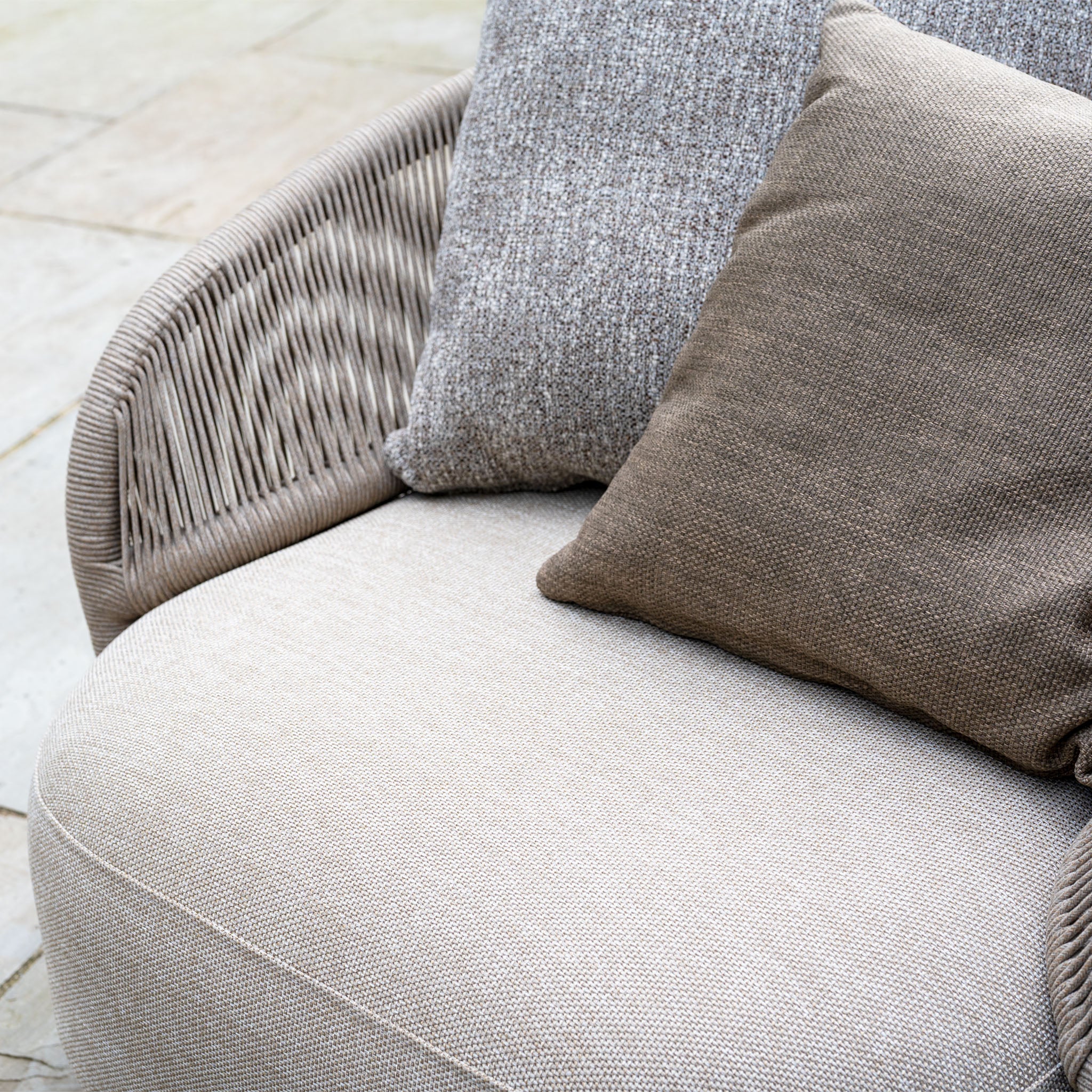 Close-up of the Avola Swivel Armchair in Fawn, an outdoor chair with two textured cushions—one gray, one brown—in weather-resistant Olefin, shown on a stone patio.