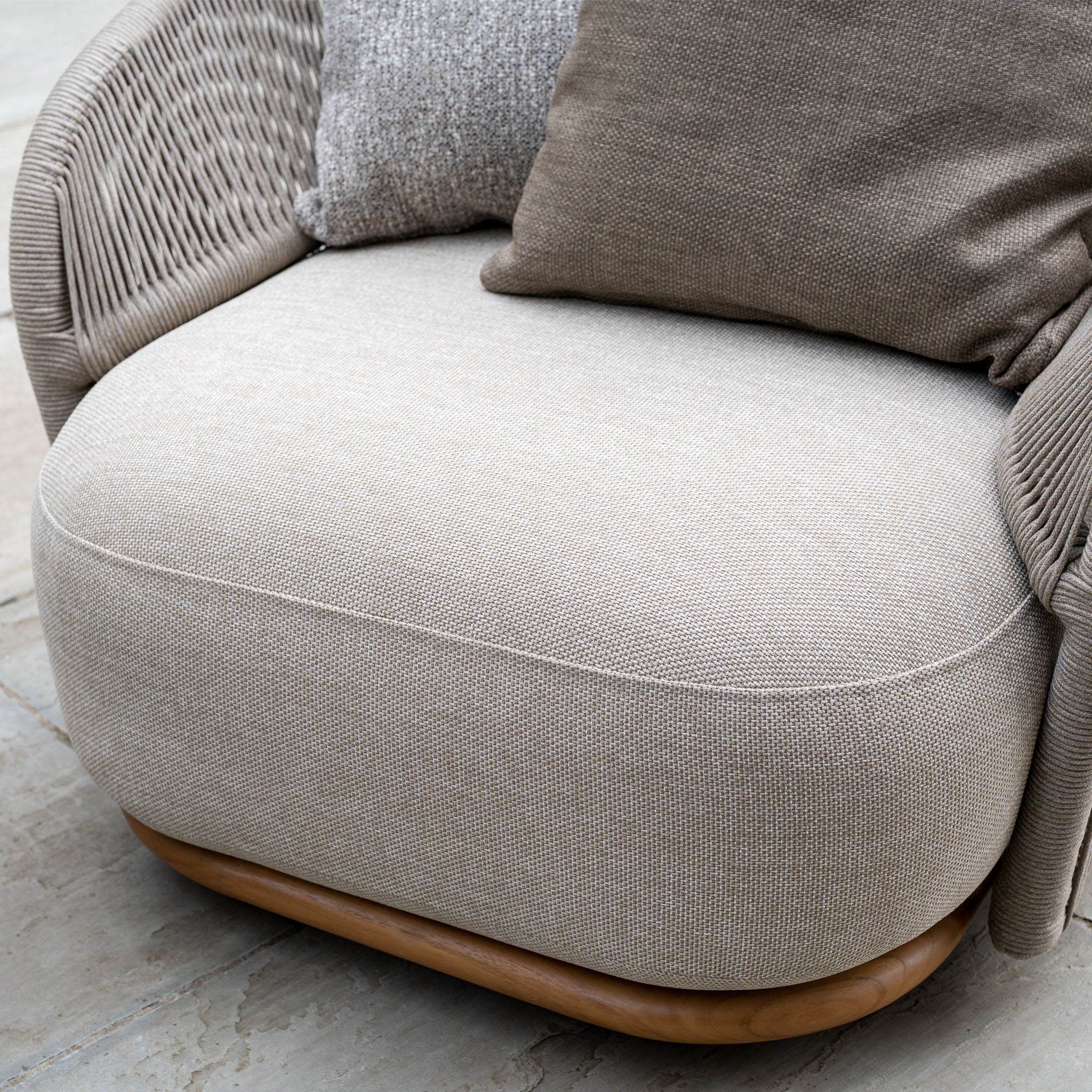 Close-up of the Avola Swivel Armchair in Fawn, an outdoor chair with weather-resistant beige Olefin upholstery, textured cushions, and a durable wooden base.