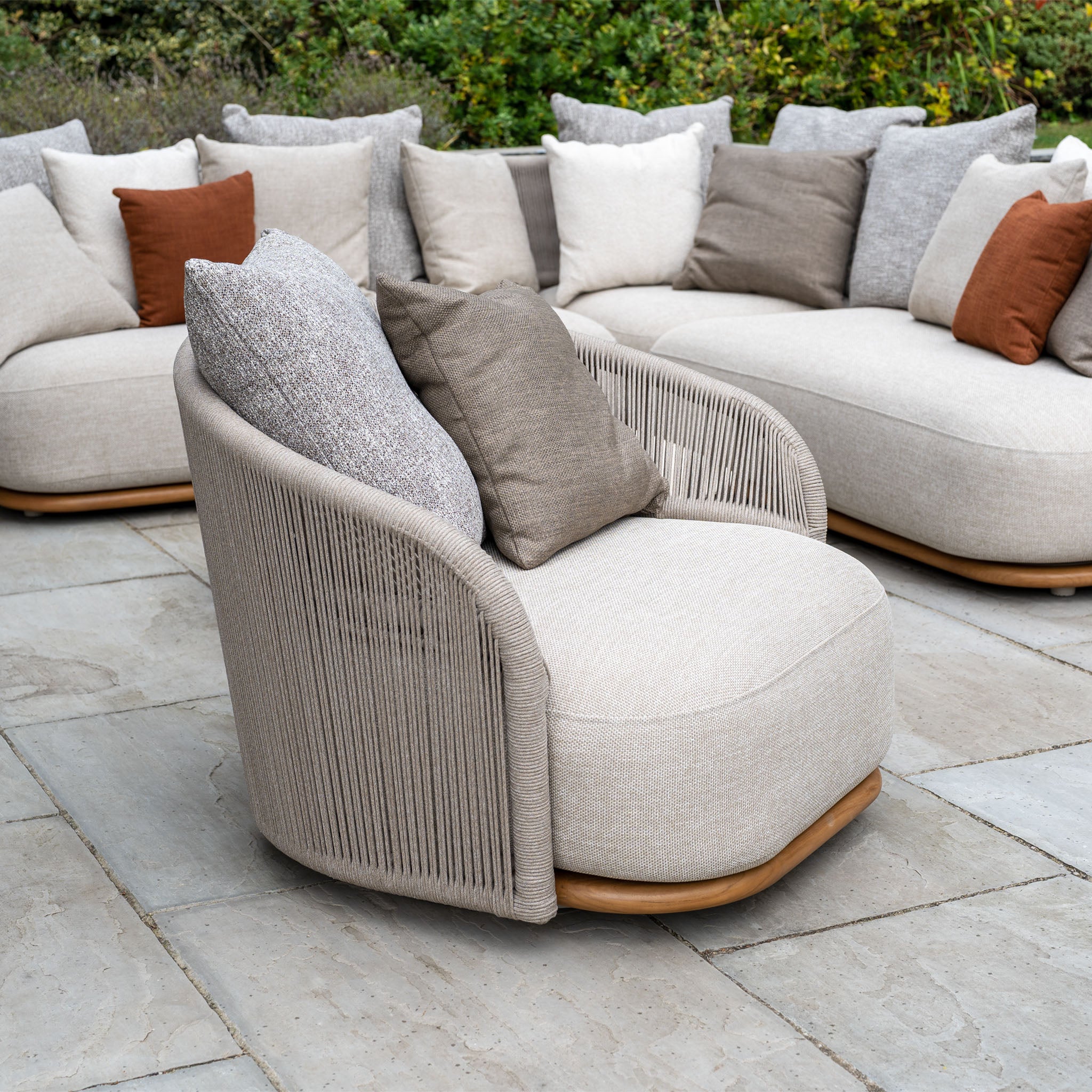 The Avola Swivel Armchair in Fawn features neutral and brown cushions, weather-resistant Olefin fabric, and complements stone patios and outdoor sofas with enduring style.