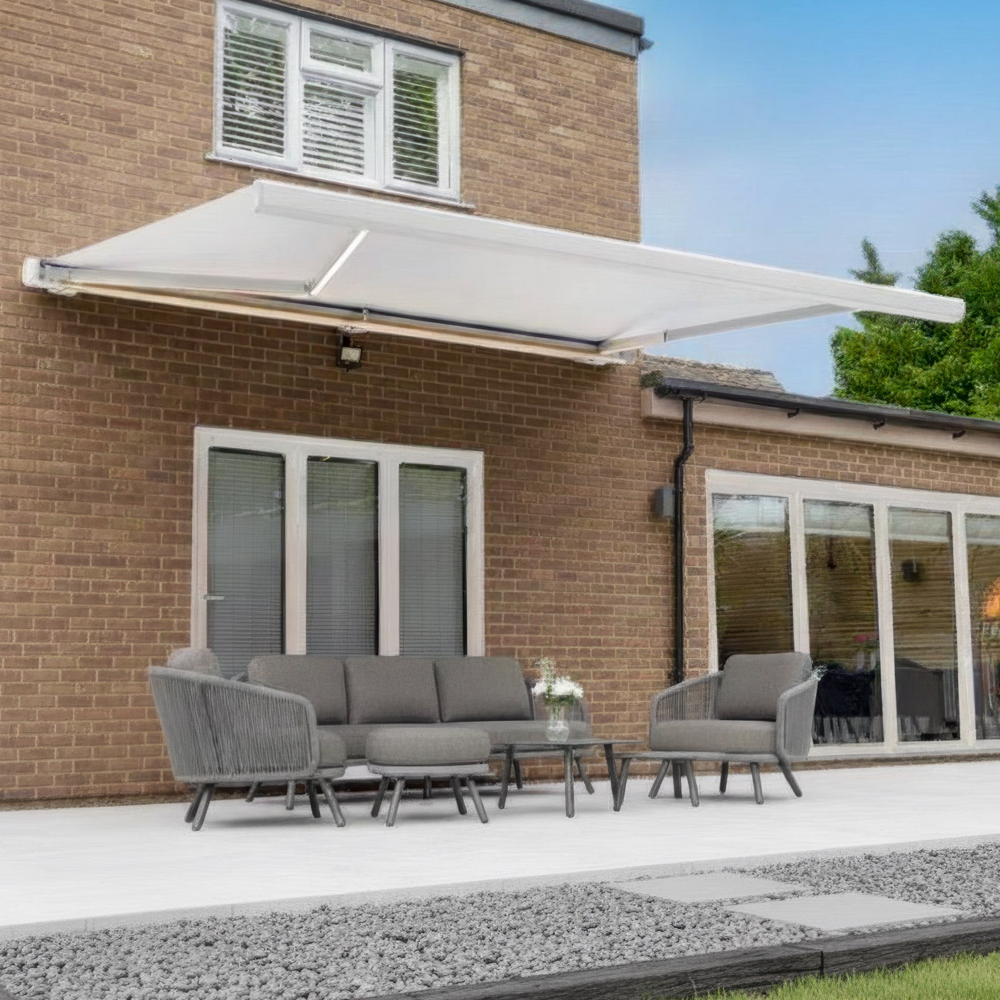 Modern patio with gray outdoor furniture beneath the 4m x 3m Electric Motorised Awning in White—waterproof, seamlessly retractable, and attached to a brick house.