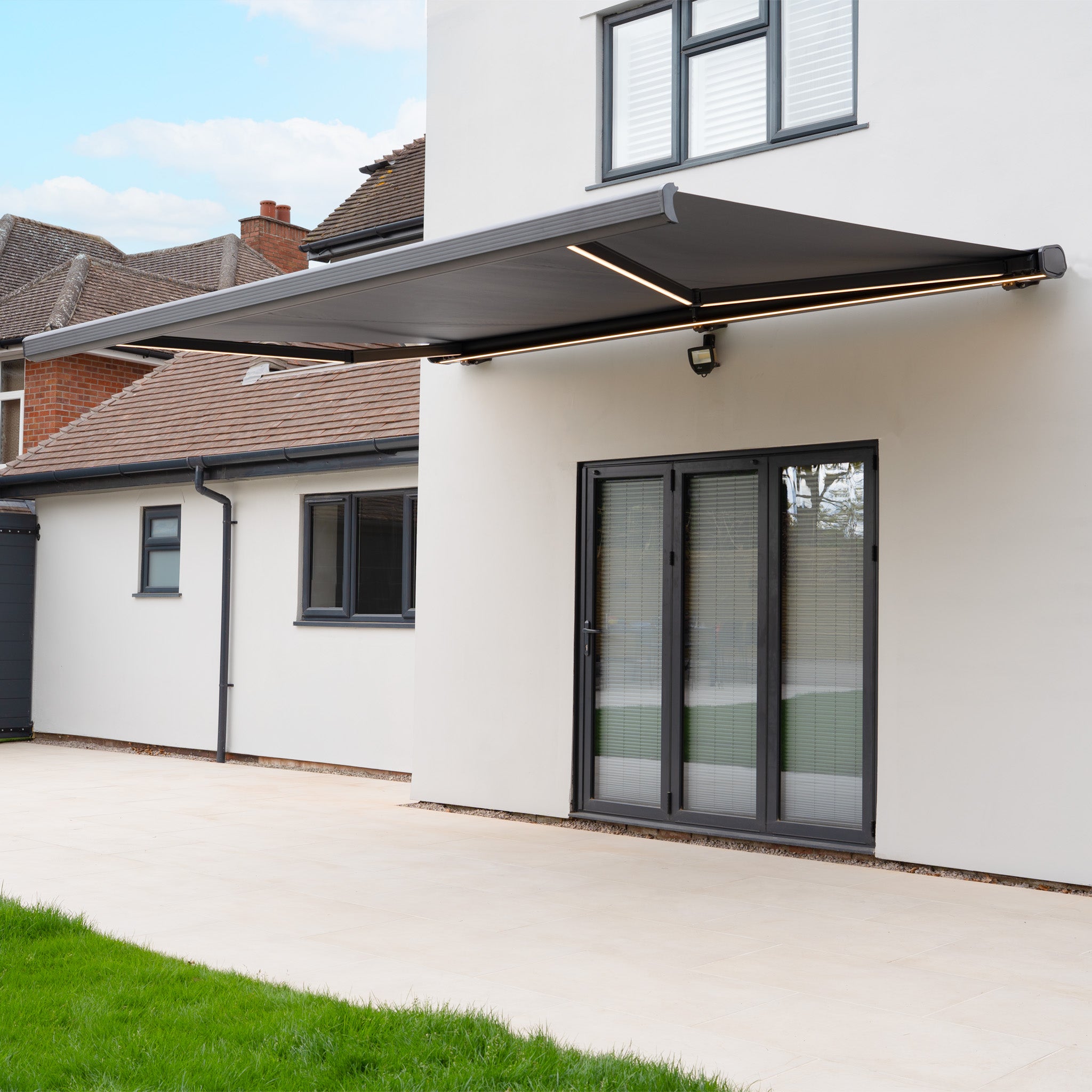 A modern house with a 3m x 2m Electric Motorised Awning in Grey, made from waterproof acrylic fabric, installed above glass patio doors.