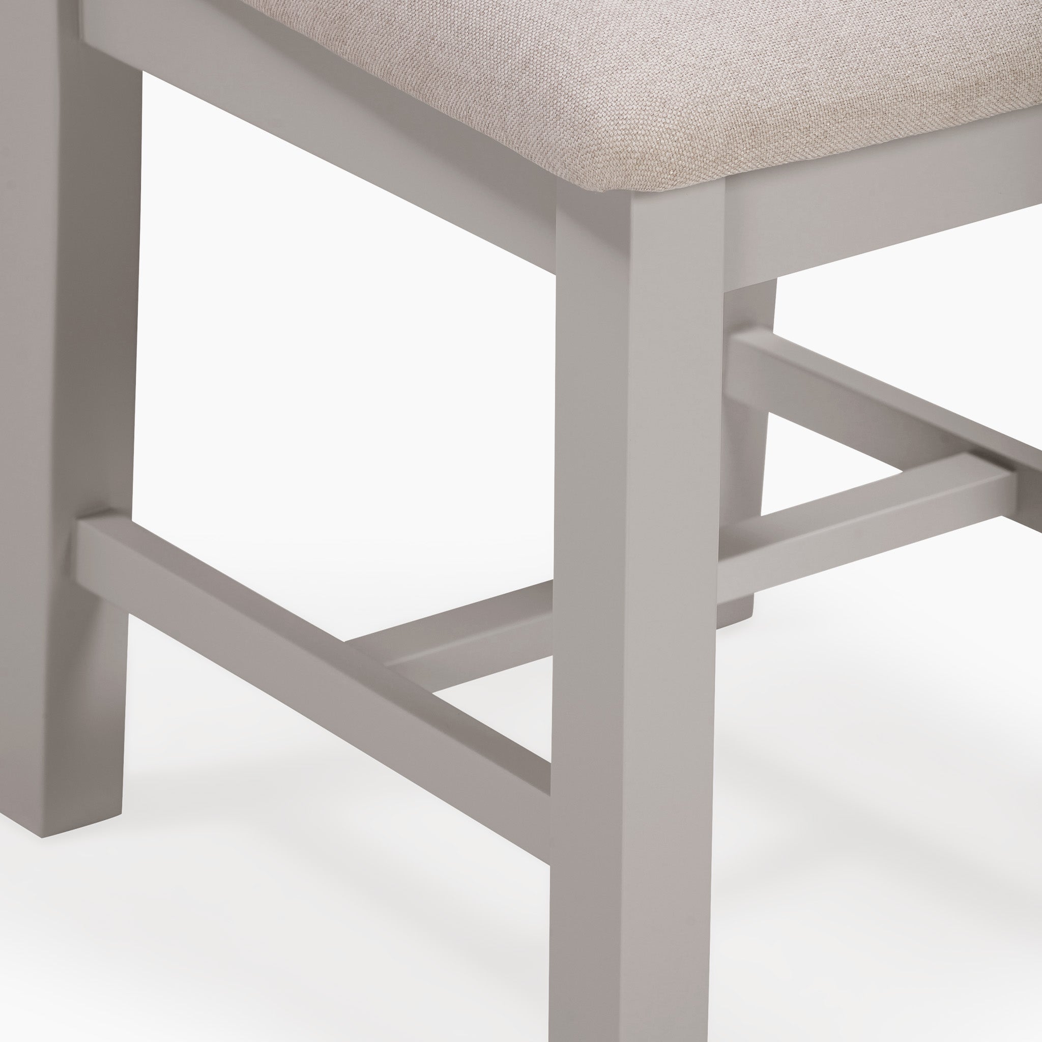 Close-up of a light gray wooden chair leg with a beige cushioned seat, perfectly complementing the Pebble Grey finish of the Burford 6 Seat Extending Dining Set.