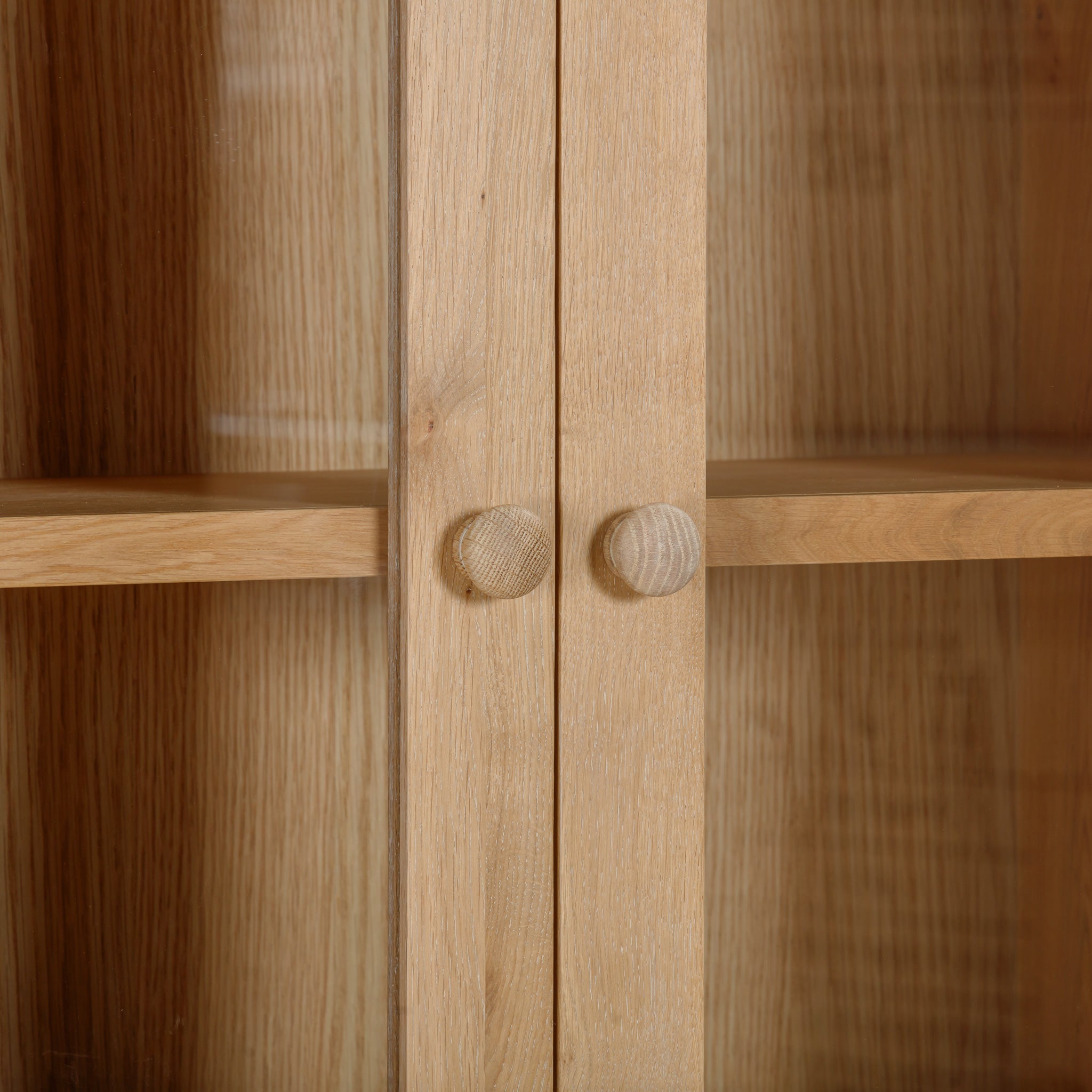 Close-up of the Burford Display Cabinet in Natural Oak, showcasing its round knobs and glass-paneled doors that reveal empty shelves inside.