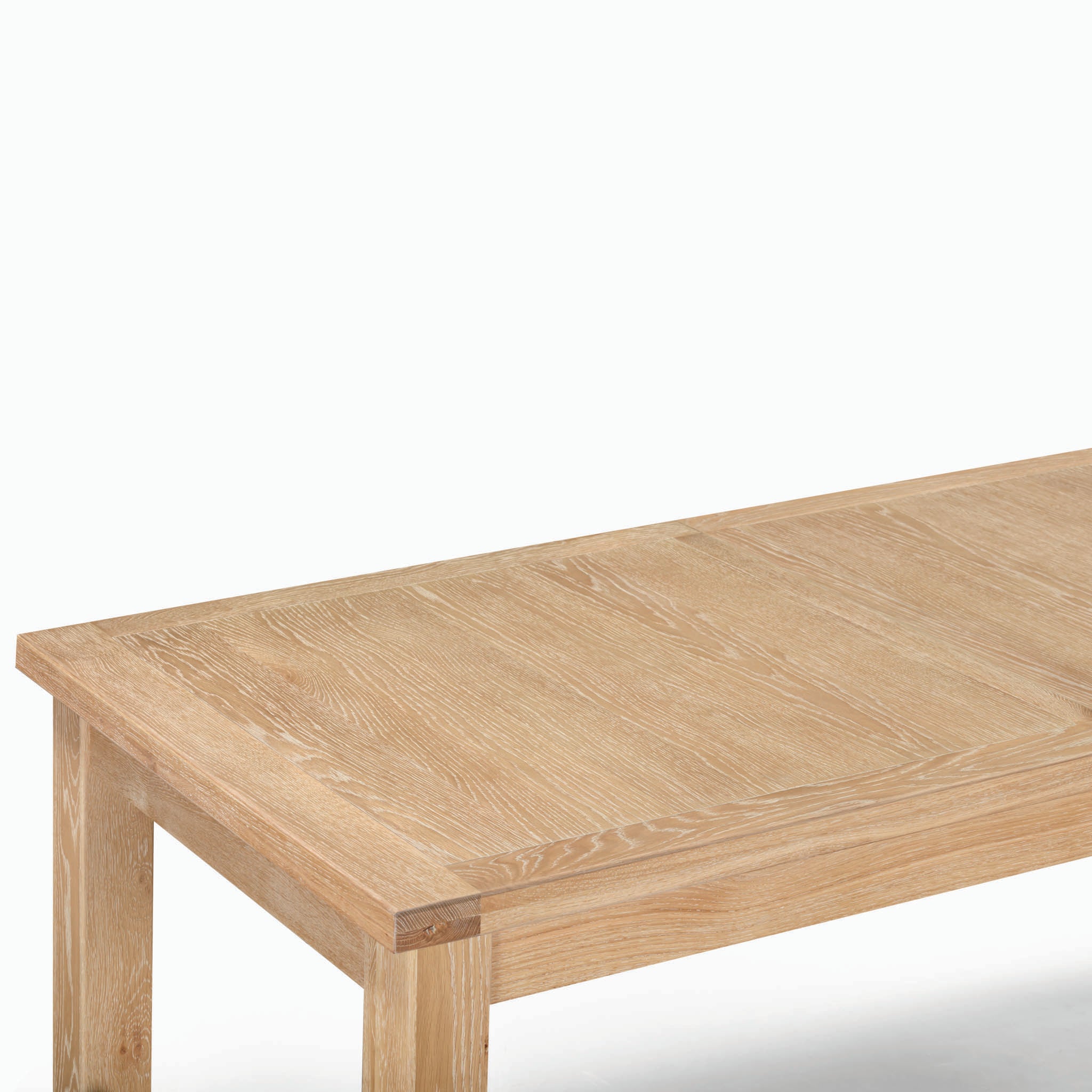 Close-up of a wooden table with a whitewash finish, highlighting the tabletop and corner's wood grain, showcasing the natural oak allure of the Burford 8 Seat Extending Dining Set.
