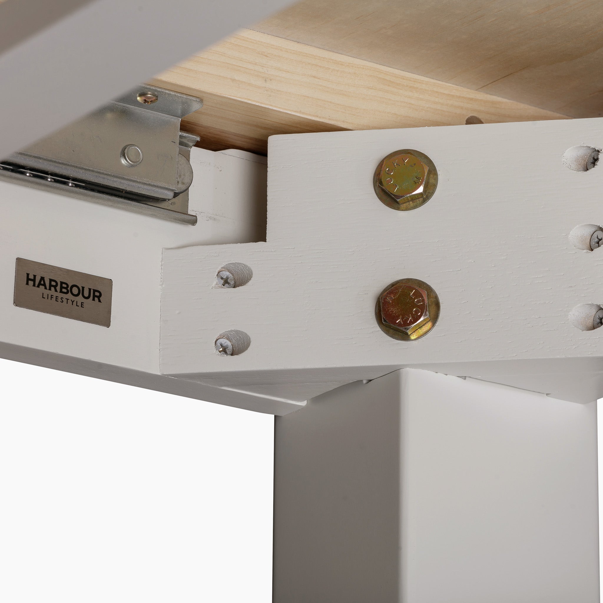 Close-up of a white wooden table corner with metal bolts and the "Harbour Lifestyle" label, reminiscent of the timeless elegance of the Burford 6 Seat Extending Dining Set in Pebble Grey, ideal for enhancing dining spaces with effortless style.