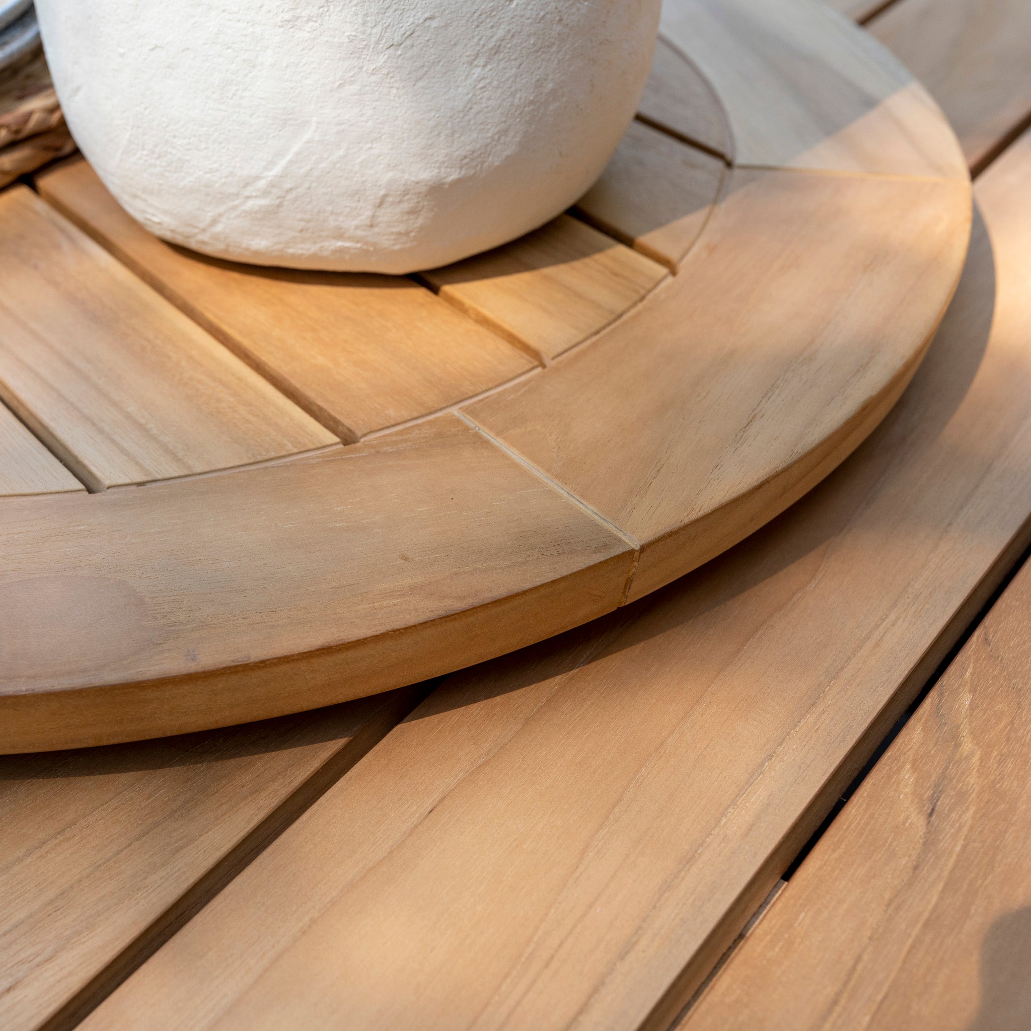 Close-up of the Puccini 6 Seat Round Dining Set with Lazy Susan in Latte, featuring a large, circular wooden lazy Susan on a slatted teak wood table with a white ceramic pot on top.