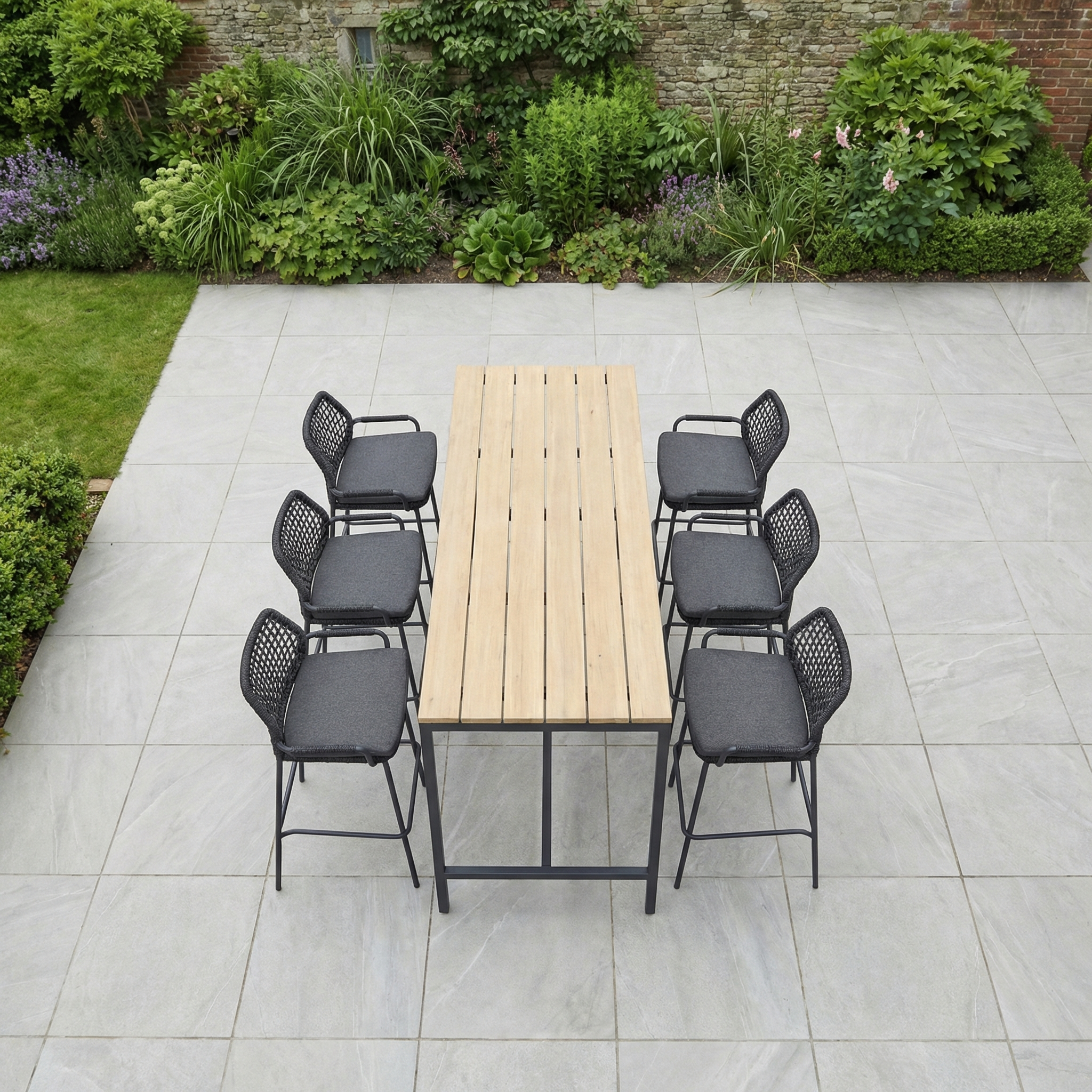 The Barista 6 Seat Bar Set with Teak Table in Anthracite from our rope collection sits on a tiled patio surrounded by greenery—perfect outdoor furniture for stylish gatherings.