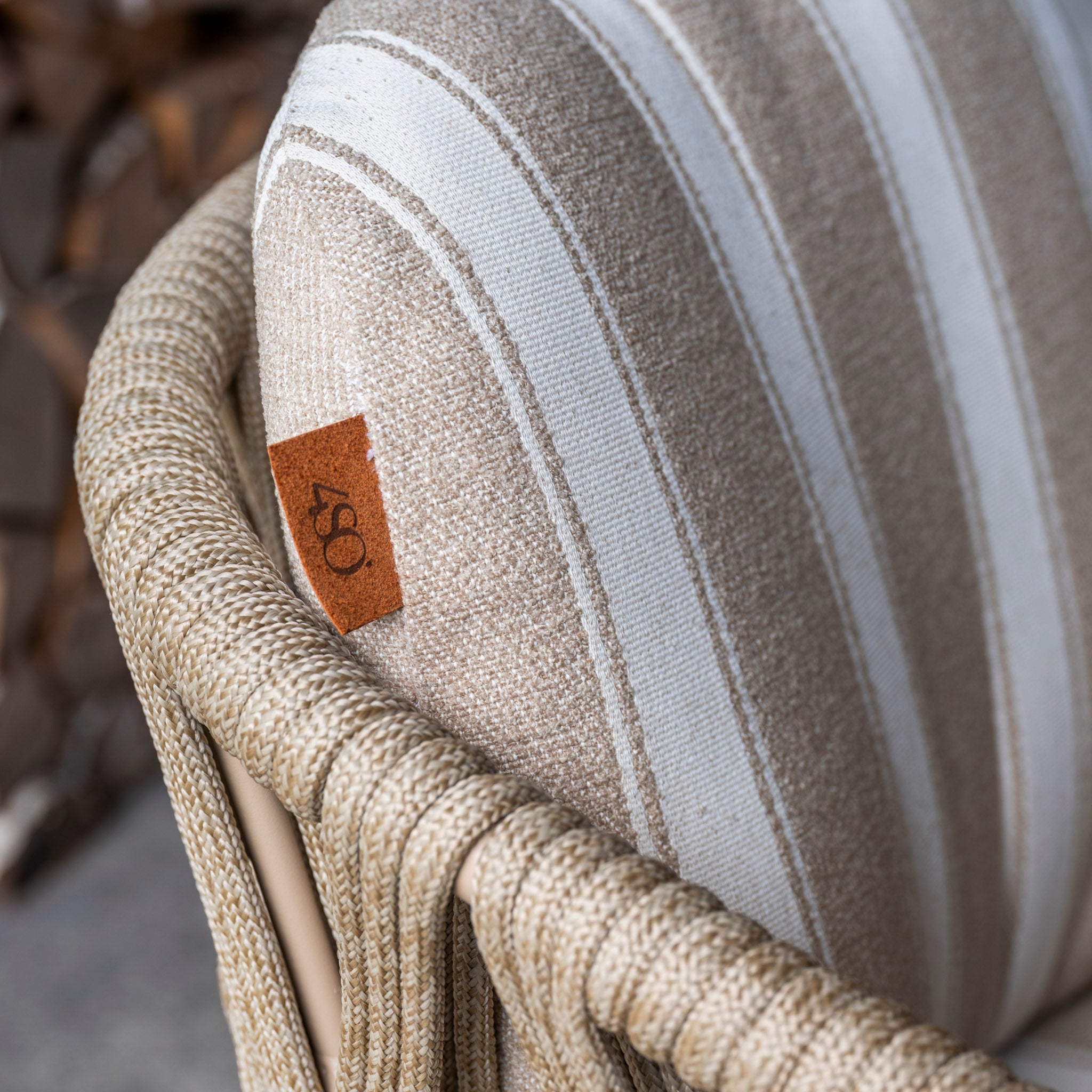 Close-up of a beige and white striped cushion on a woven chair from the Madeira 6 Seat Curved Rectangular Dining Set in Striped Latte, featuring a small brown tag.