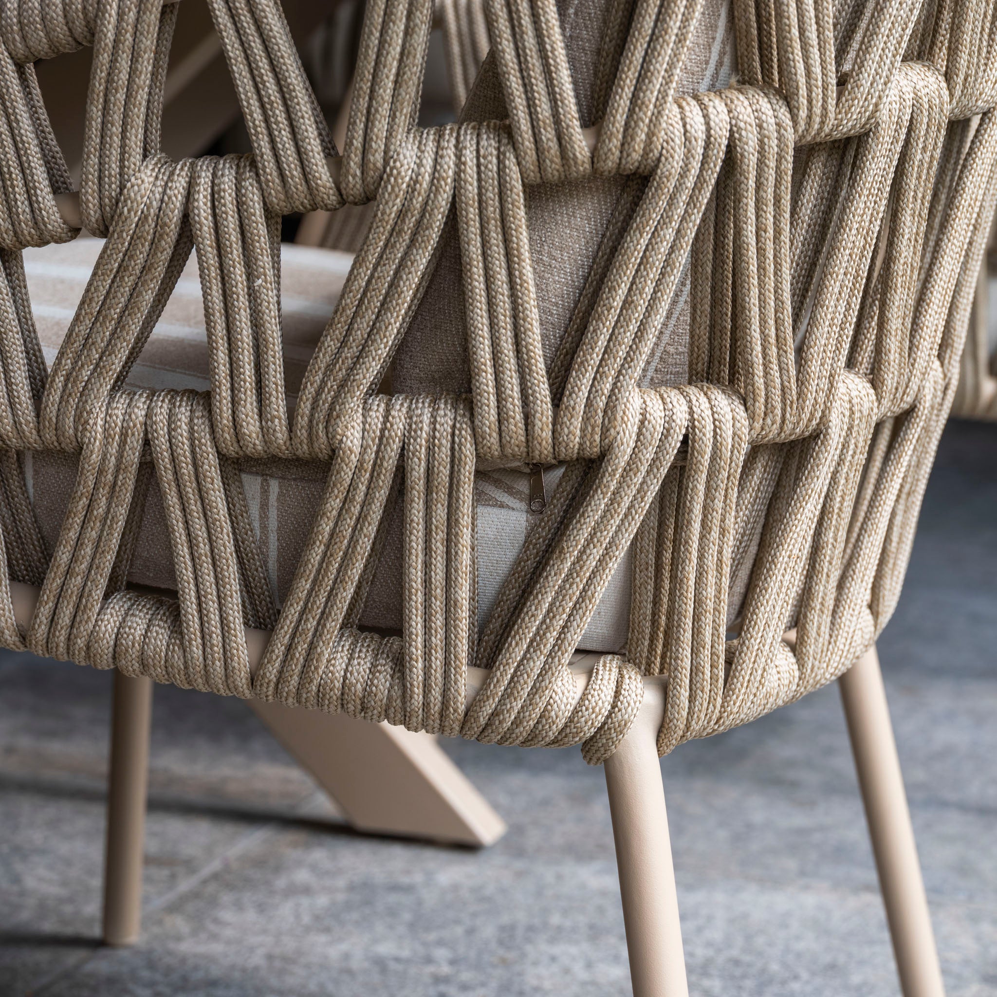 Close-up of the Madeira 6 Seat Curved Rectangular Dining Set in Striped Latte, featuring a curved dining chair with thick beige woven rope over a light cushion and metal legs on stone—ideal for outdoor dining.