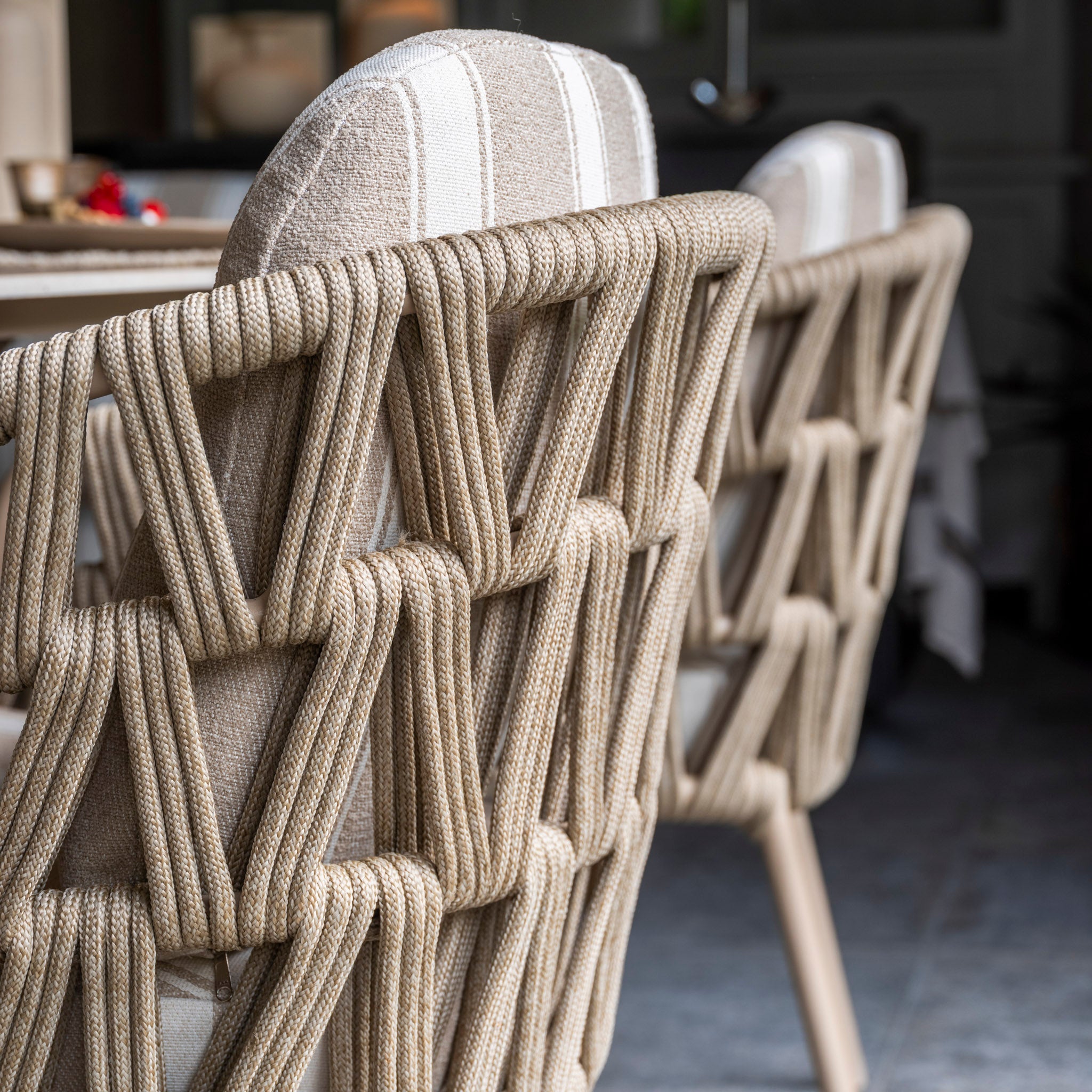 Close-up of the Madeira 6 Seat Curved Rectangular Dining Set in Striped Latte, featuring beige-cushioned curved chairs with woven rope backs, arranged around a powder-coated aluminium table indoors.
