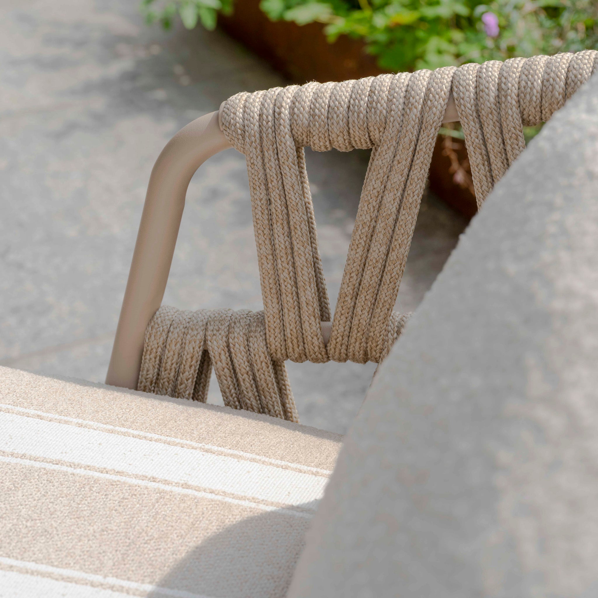 Close-up of a beige garden furniture piece with woven rope and a striped seat cushion from the Madeira 3 Seat Sofa Set in Striped Latte, placed on a stone patio.
