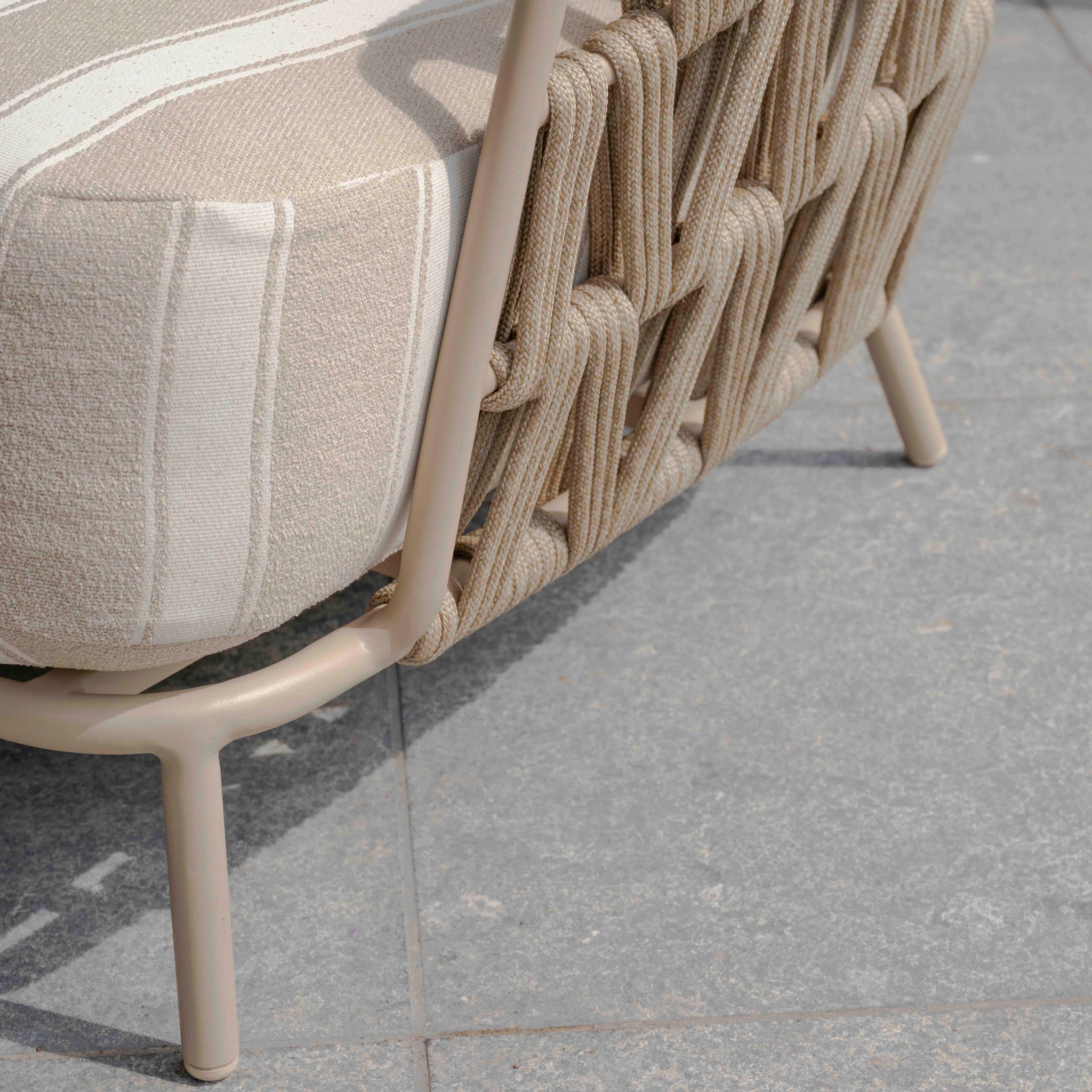 Close-up of a woven outdoor chair from the Madeira 3 Seat Sofa Set in Striped Latte, featuring a striped cushion on gray tiles and highlighting stylish garden furniture.