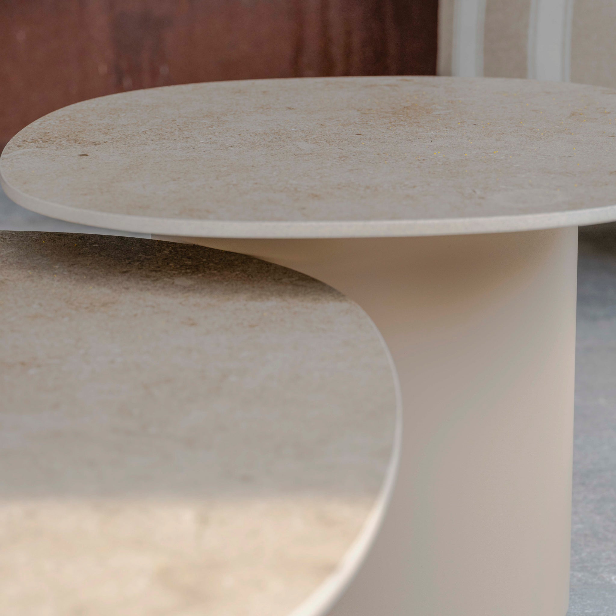 The two round beige stone tabletops with smooth surfaces and minimalist cylindrical bases perfectly complement the Madeira 3 Seat Sofa Set in Striped Latte, enhancing any modern garden or outdoor space.