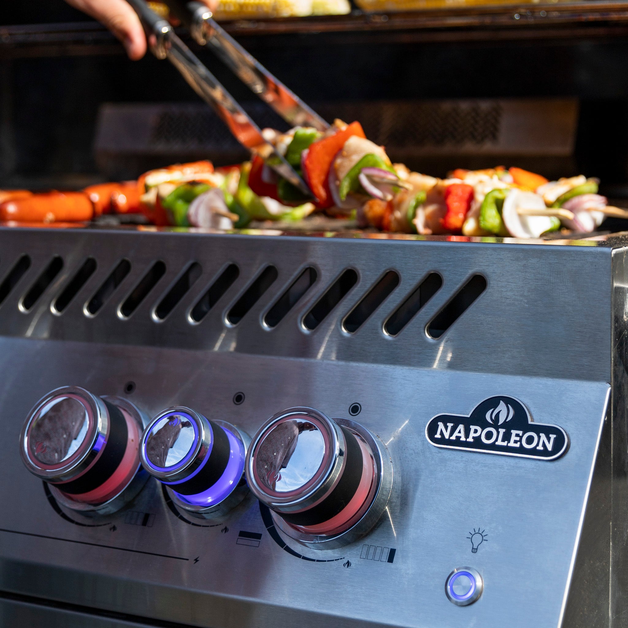 A person is grilling vegetable and meat skewers on a Napoleon 700 Series 38" Built-in Gas Grill, enjoying the perfect heat distribution provided by the JETFIRE ignition system.