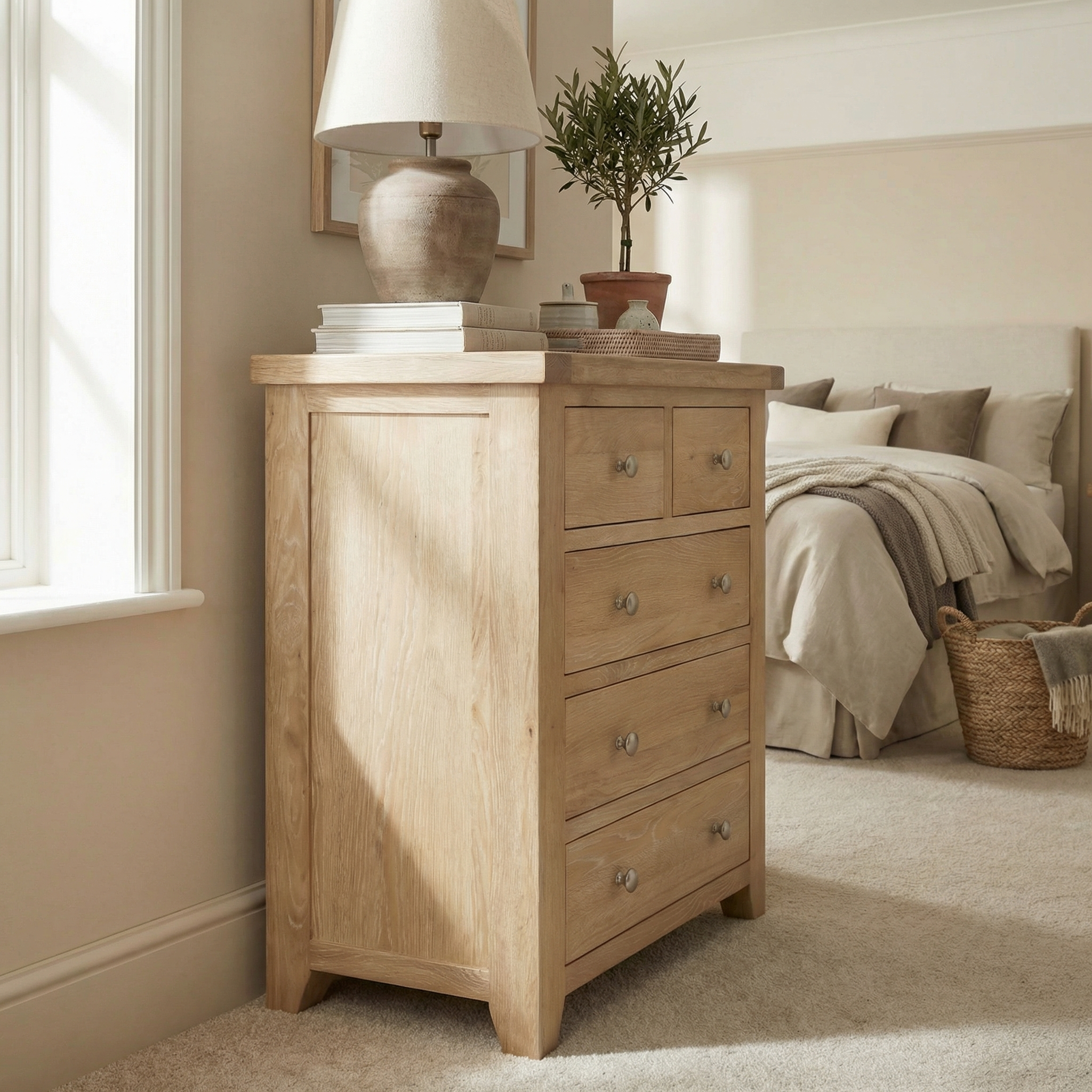 The Burford 2 Over 3 Chest of Drawers in Natural Oak, styled with a lamp and potted plant, offers a cozy and practical storage solution for neutral-toned bedrooms or any space.