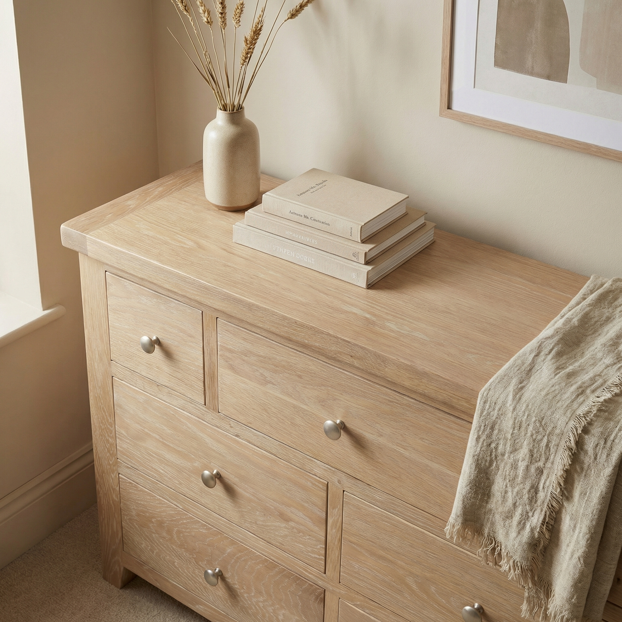 The Burford 3 Over 4 Chest of Drawers in Natural Oak, styled with books, dried plants, and a beige throw in a neutral-toned room—ideal oak storage furniture for a warm, organized home.