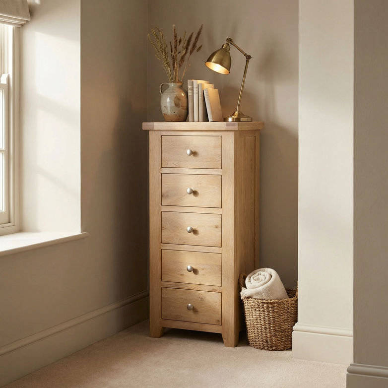 The Burford 5 Chest of Drawers in Natural Oak brings cozy charm and practical bedroom storage to any softly lit corner, beautifully styled with a lamp, vase, and basket.