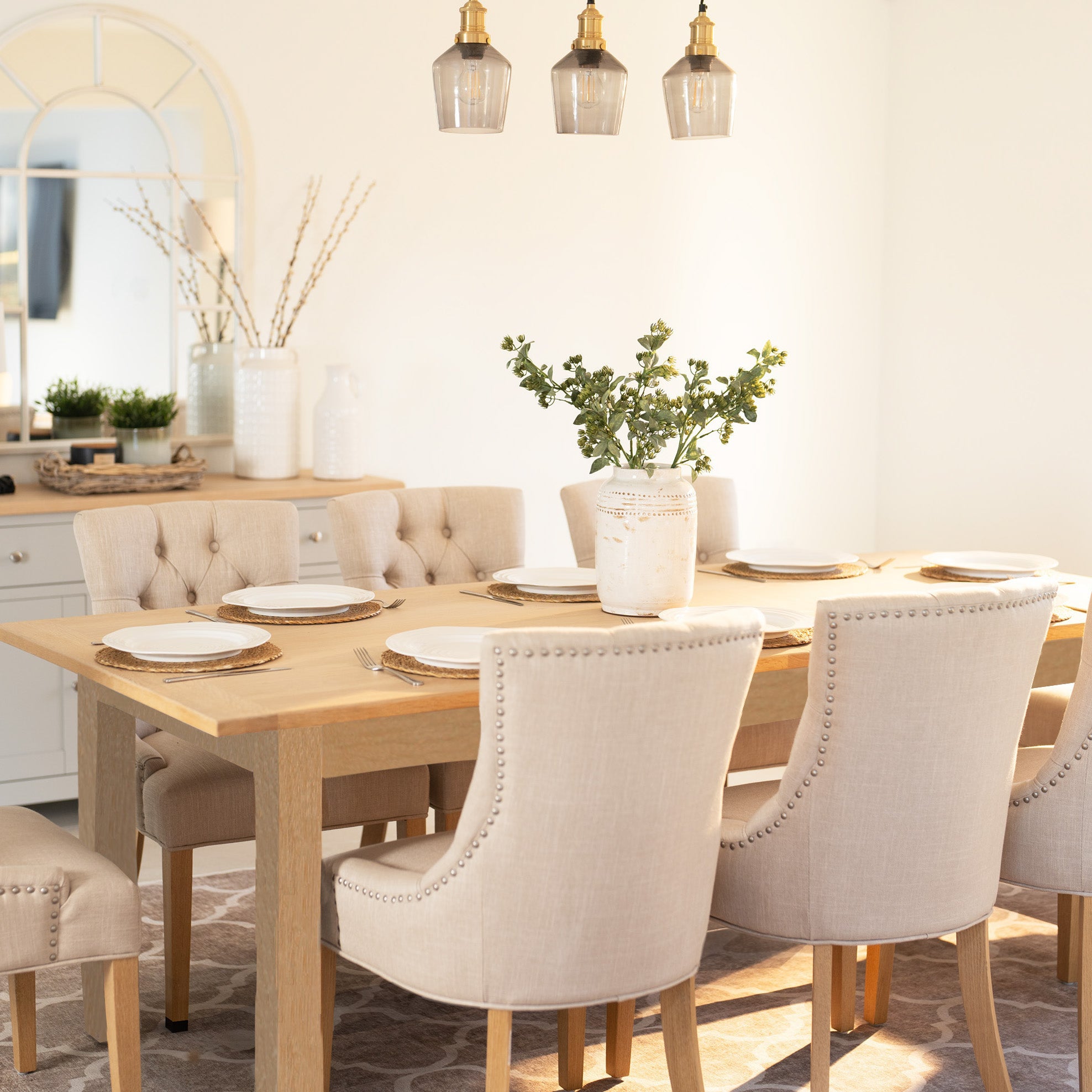Bright dining room with the Burford 8 Seat Extending Dining Set featuring Regent Chairs in natural oak and ivory, with a wooden extendable table, cushioned chairs, and a greenery-filled vase centerpiece.
