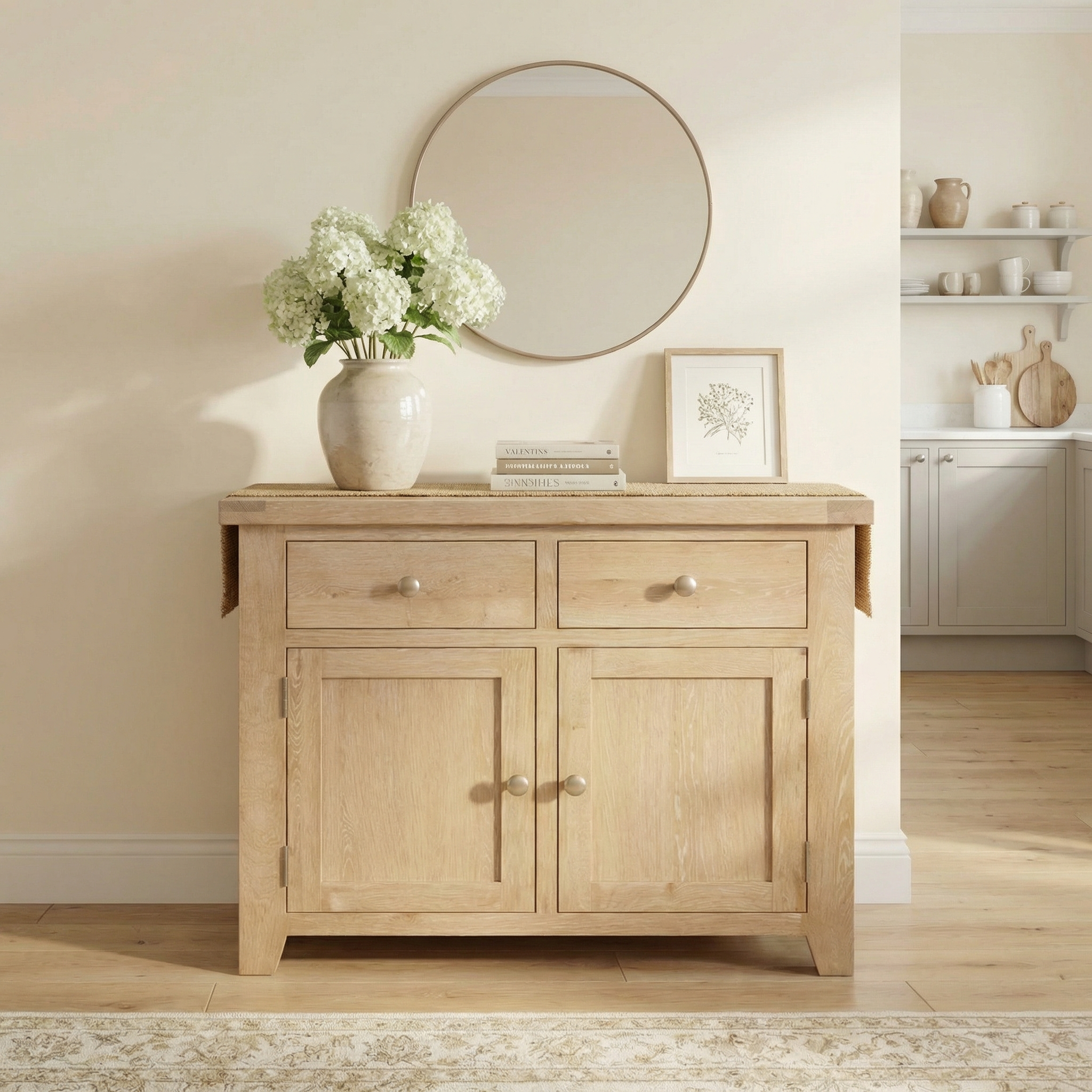 Burford 2 Door 2 Drawers Sideboard in Natural Oak styled with flowers, books, and framed art beneath a round mirror in a neutral-toned room.