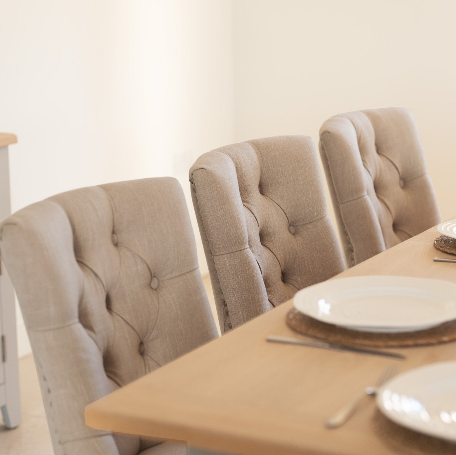 The Burford 8 Seat Extending Dining Set with Regent Chairs in natural oak and beige features tufted chairs around an extendable table, elegantly set with white plates and cutlery.